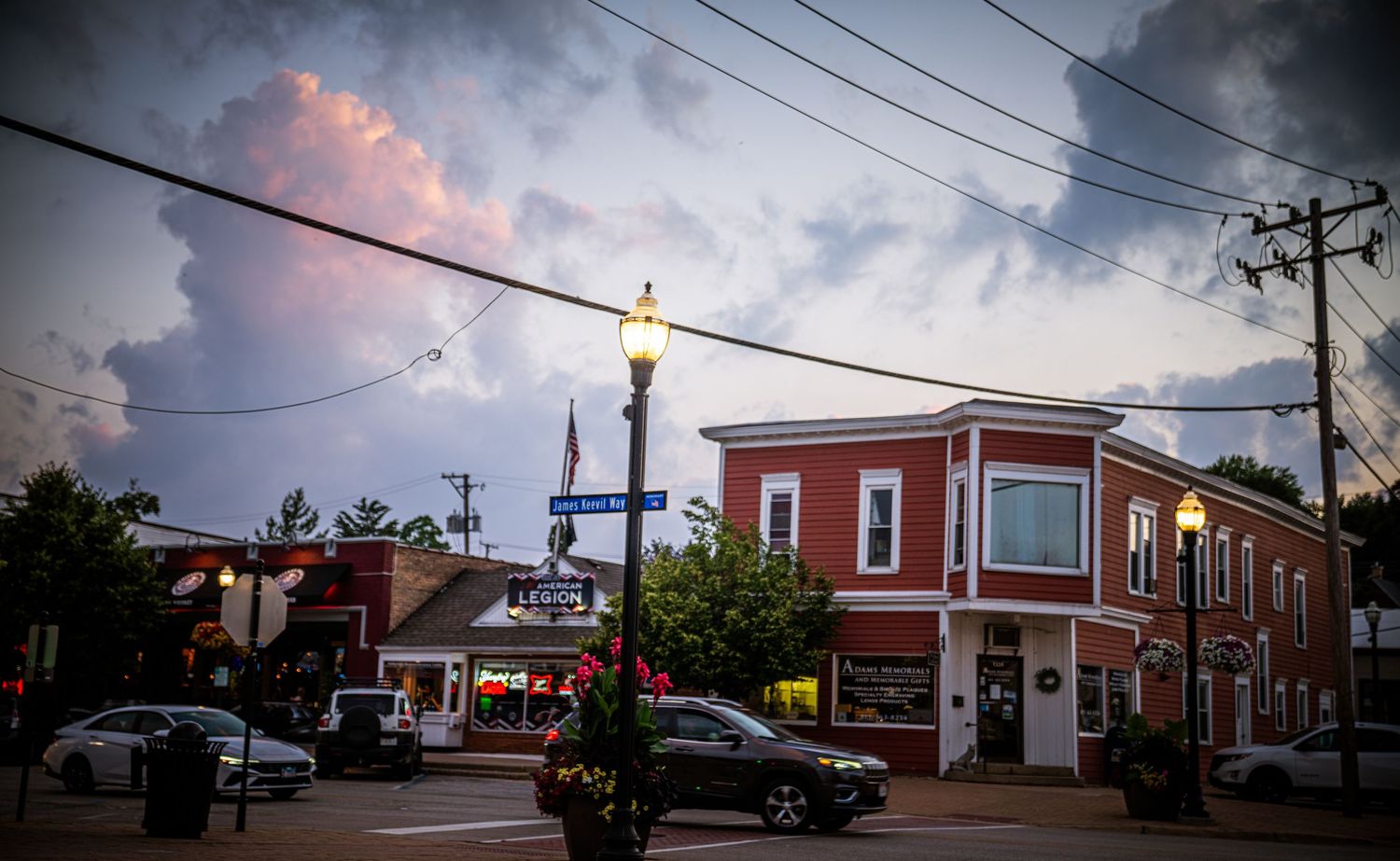 Corner brick building with decorative street lamps and power lines against dramatic evening sky.