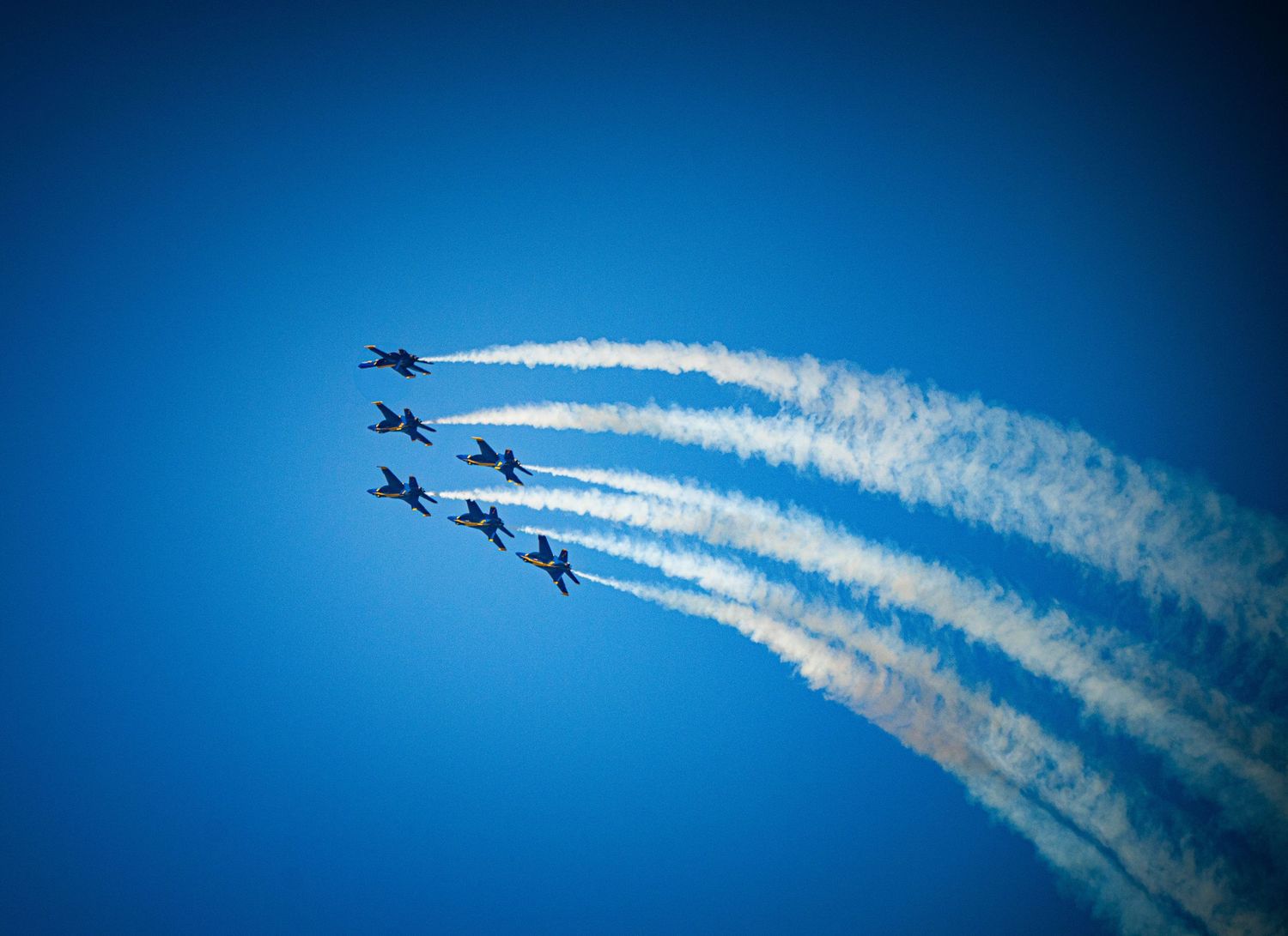 Fighter jets executing a synchronized flight pattern with white smoke trails in the blue sky.