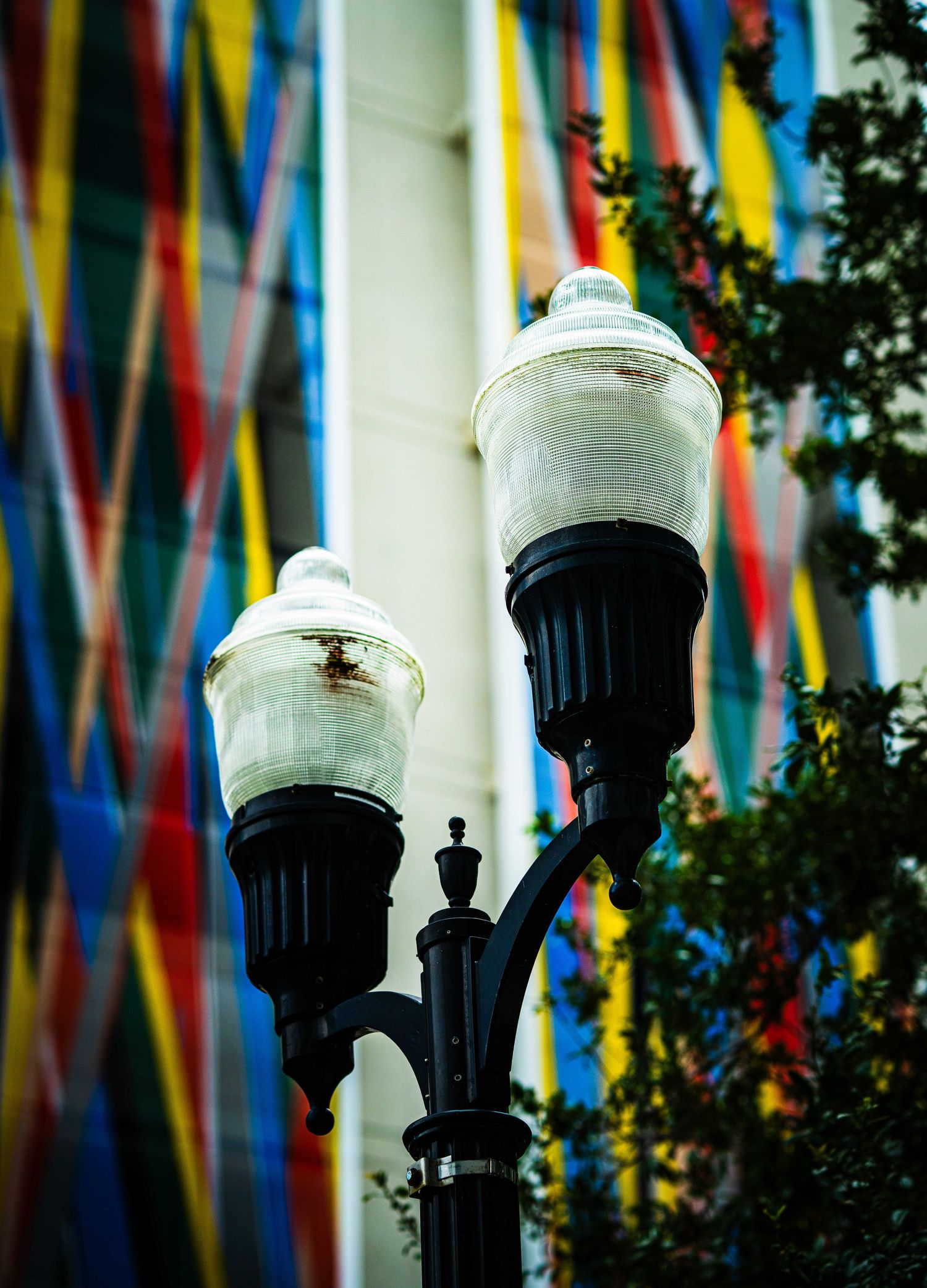 Vintage black double street lamp with colorful striped ribbons and trees in the blurred background.