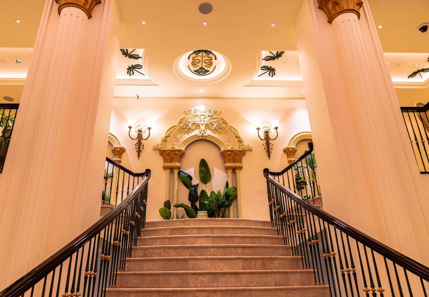 Elegant hotel grand staircase with ornate gold arch, wrought iron railings, decorative columns, and warm luxury interior lighting.