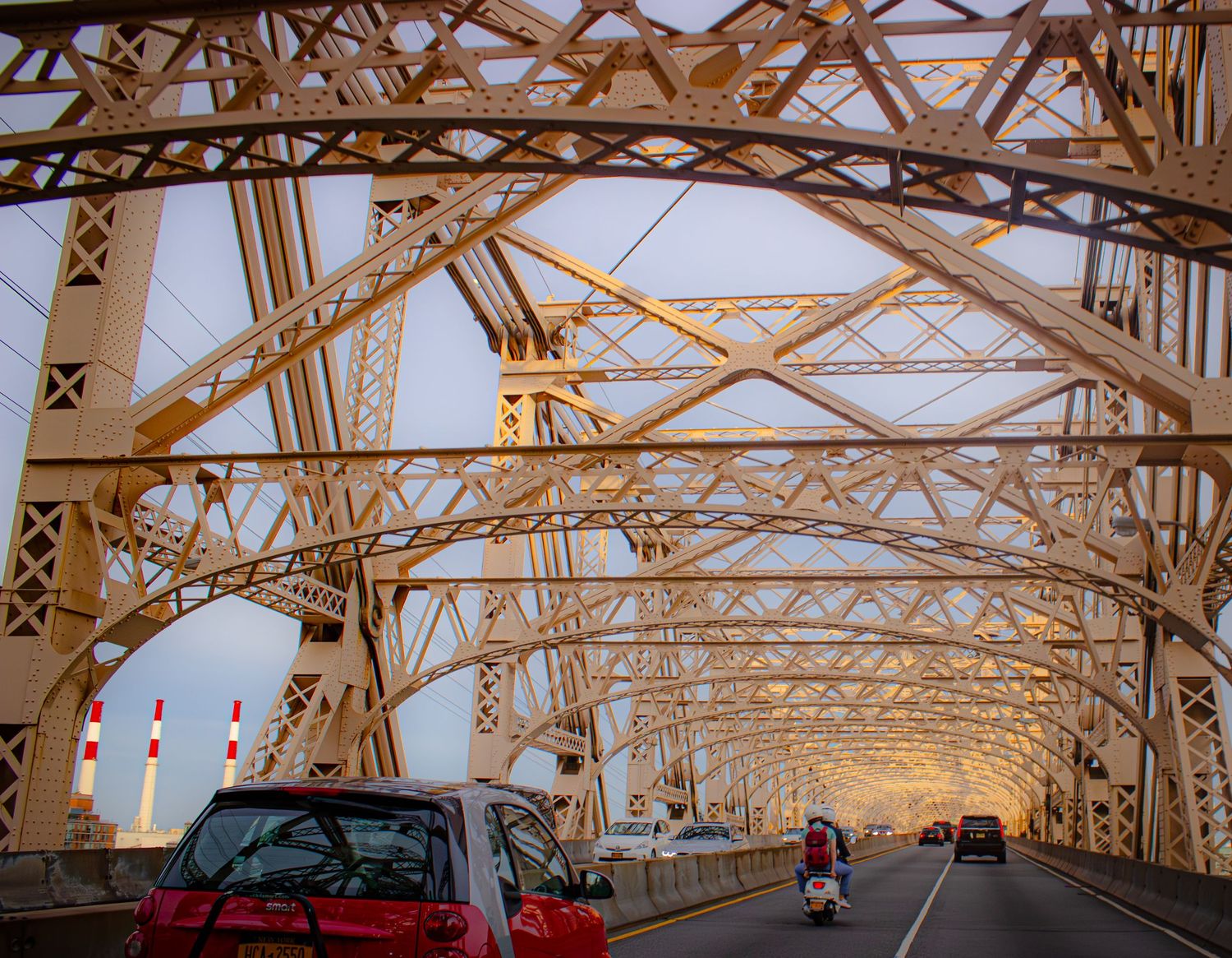 Cars drive across the Queensboro Bridge in New York City during golden hour with its iconic steel lattice structure.