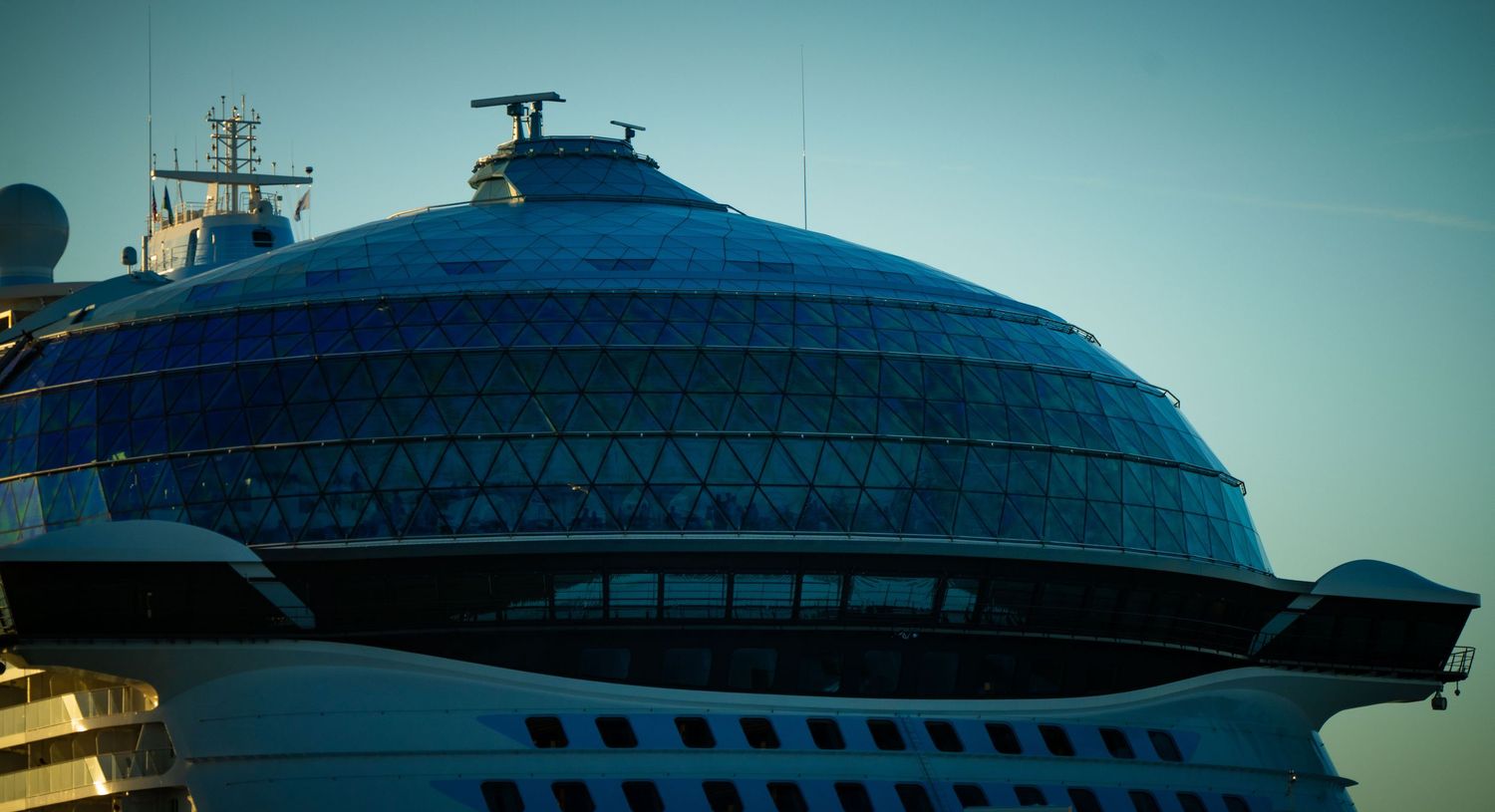 A modern cruise ship exterior with sleek architectural lines against a blue sky background.