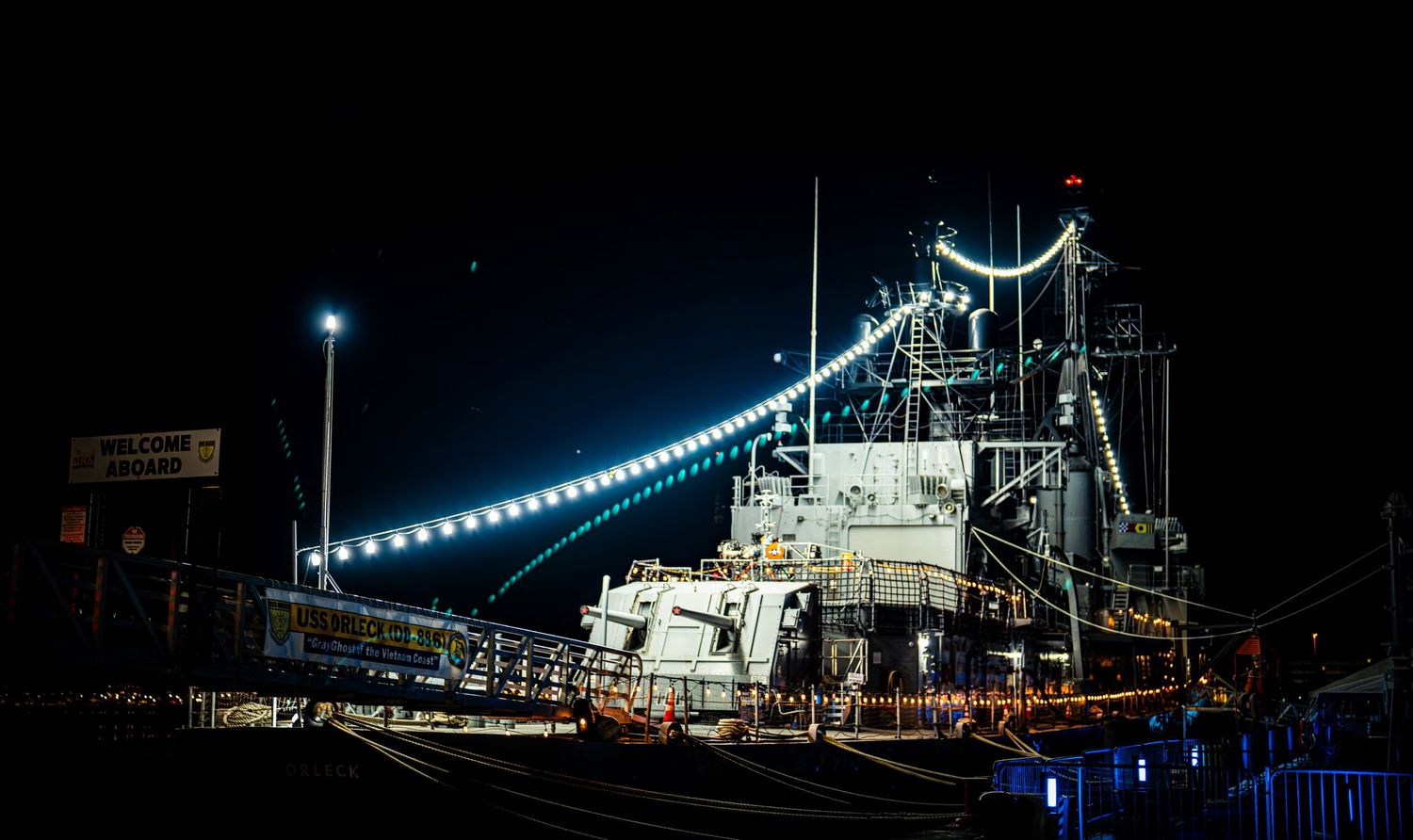 A large fishing vessel illuminated by bright lights docked at a harbor at night.