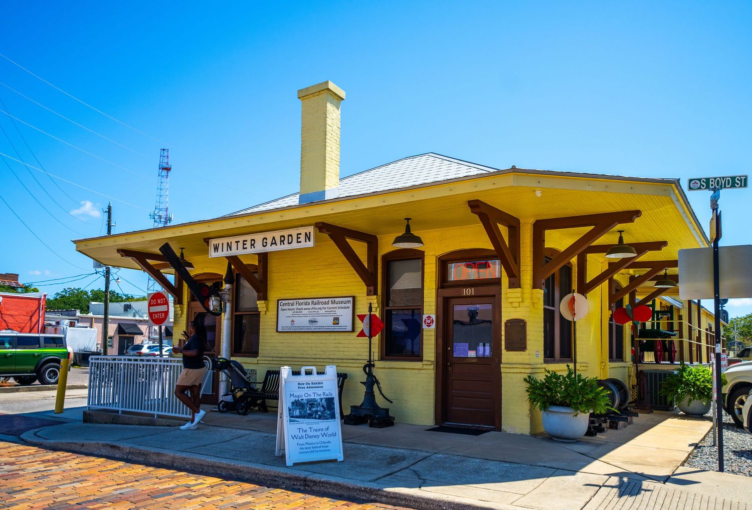 Yellow train station building exterior with red brick walkway under bright blue sky.