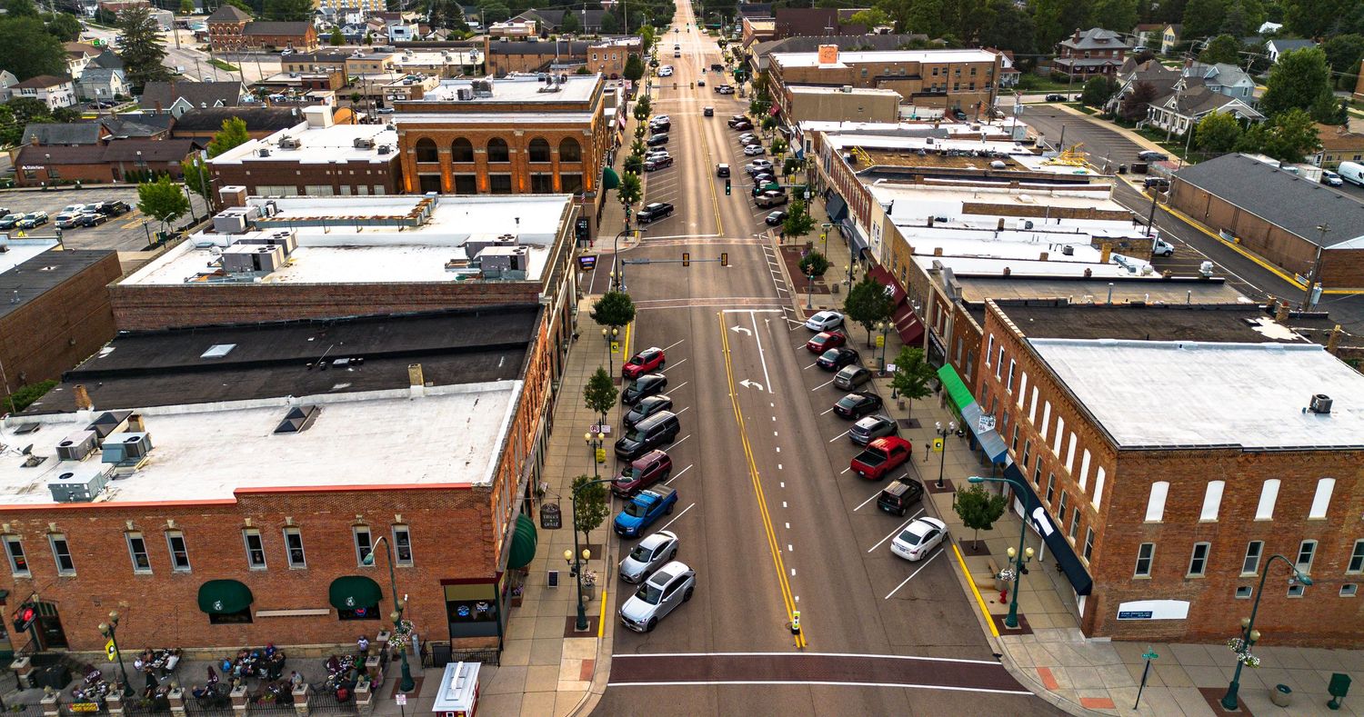 Aerial view of small town main street with brick buildings and parked cars.