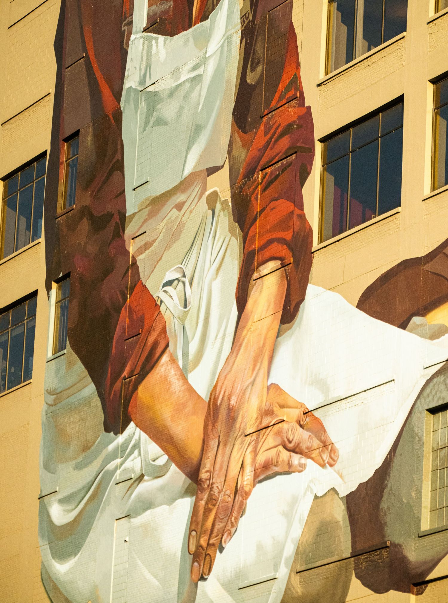 Artistic mural showing hands in warm sepia tones painted on urban building wall.