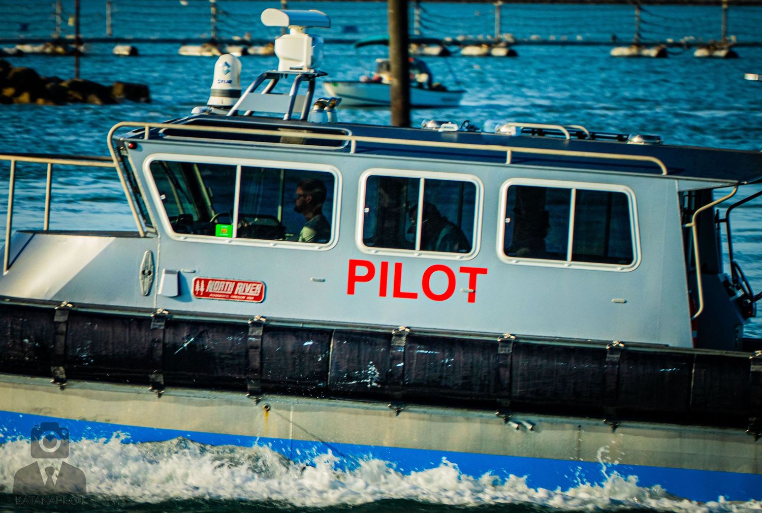 A white pilot boat cruises through bright turquoise waters near a harbor dock on a sunny day.