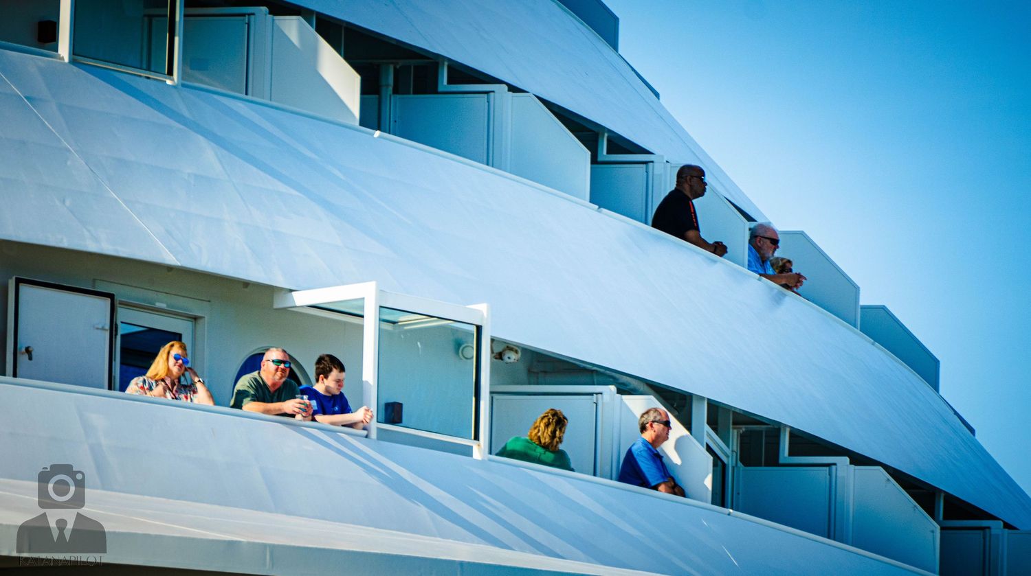 Curved white balconies of a modern building against bright blue sky with people visible on different levels.