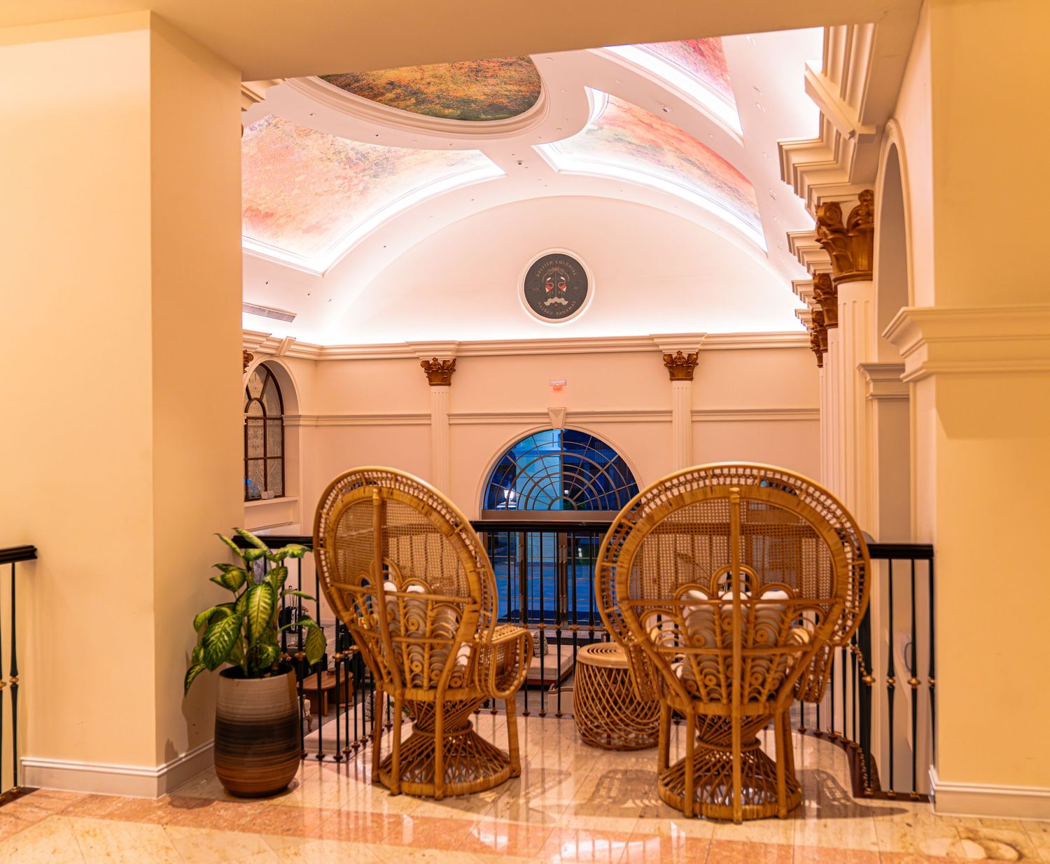 Elegant hotel lobby with rattan peacock chairs, arched ceilings, ornate columns, and warm lighting.