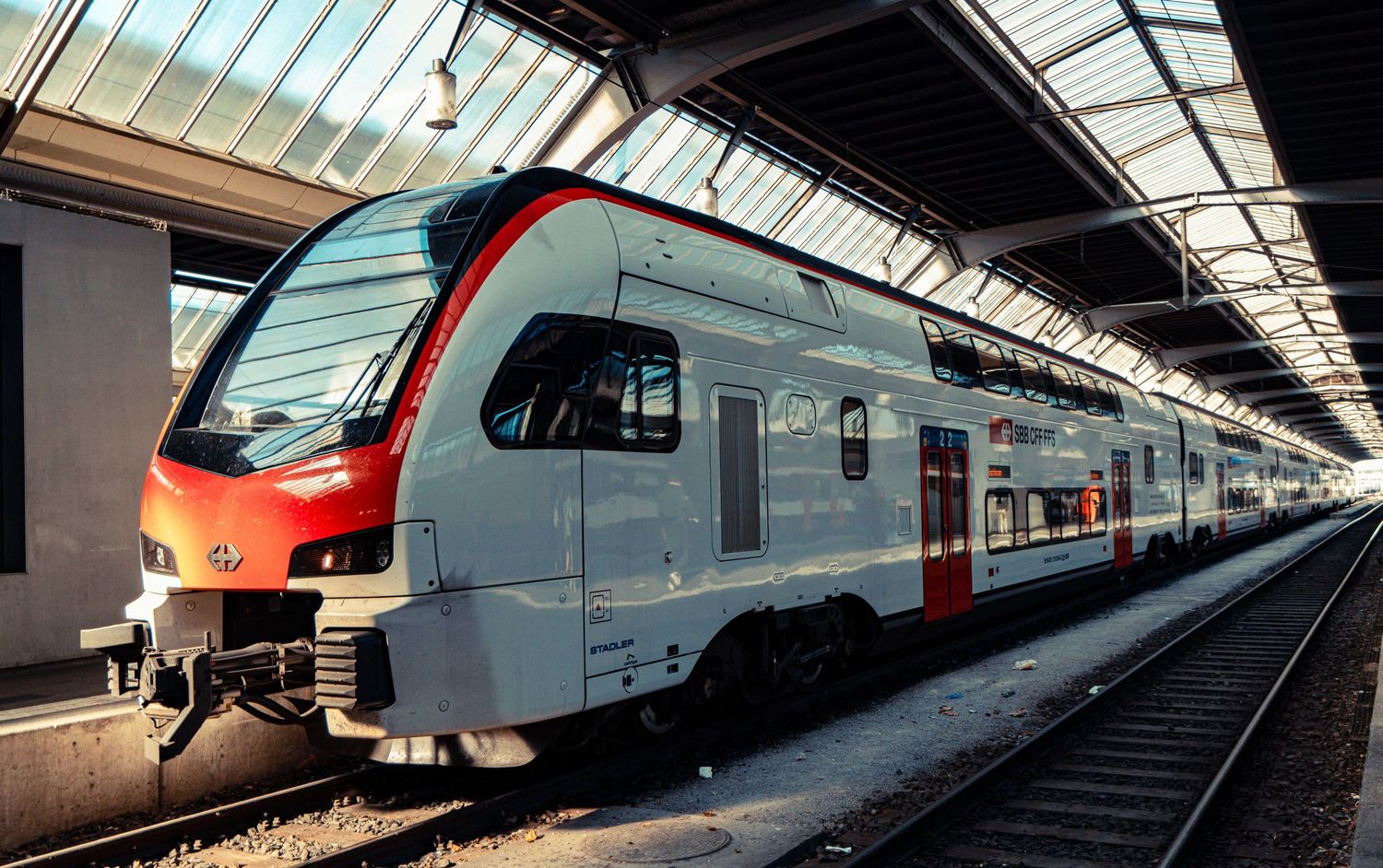 Modern red and white passenger train stopped at a covered station platform beneath a glass and steel roof.
