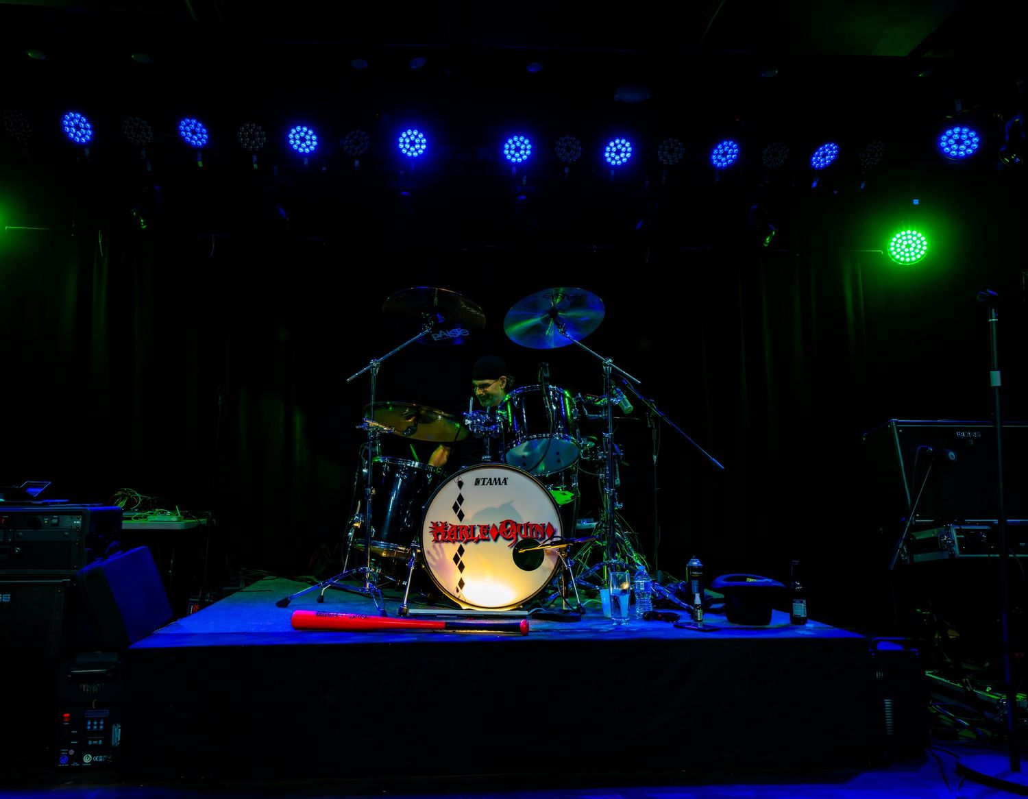 Empty concert stage with drum kit and blue overhead lights in a dark music venue.