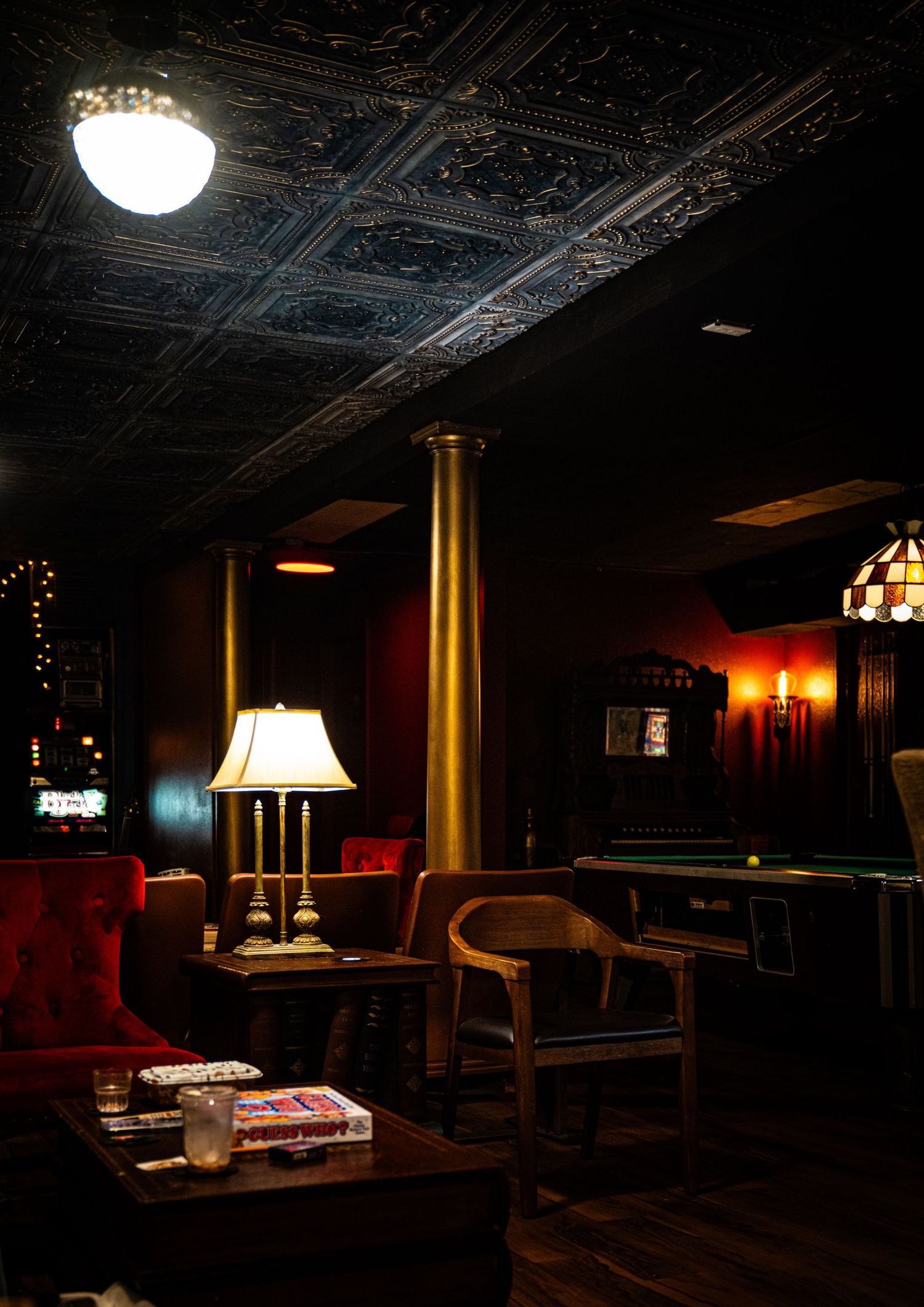 Dimly lit bar interior with vintage decor featuring ornate ceiling details, wooden furnishings and warm ambient lighting.