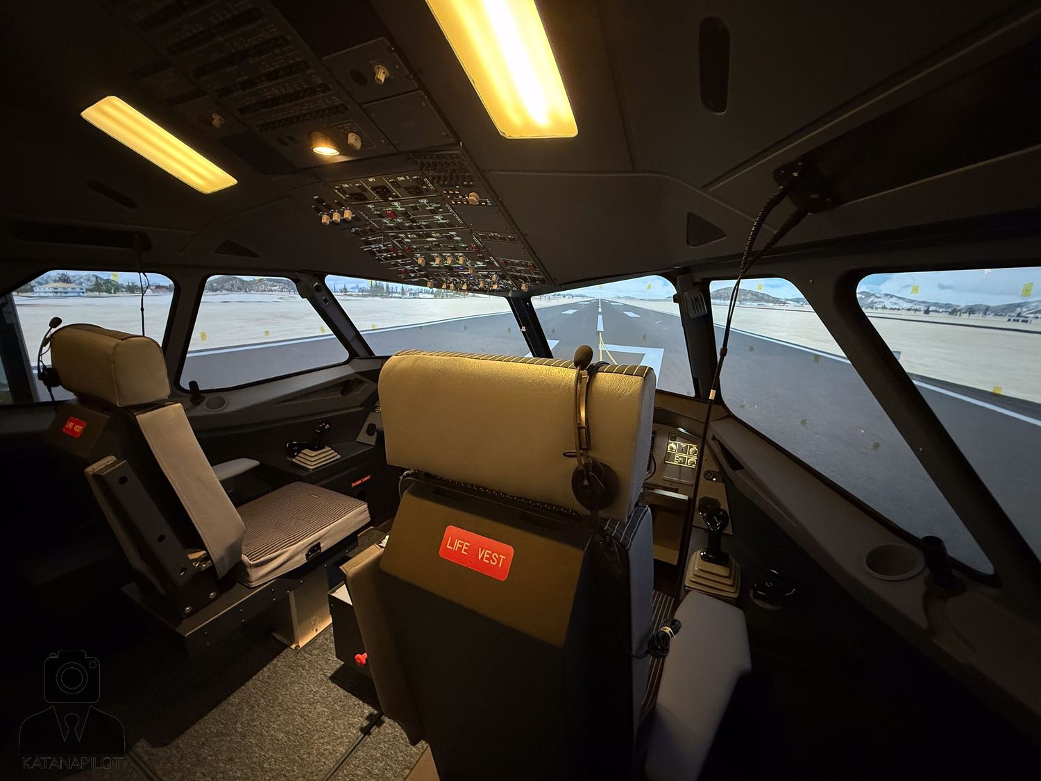 Aircraft simulator cockpit view with yellow overhead lighting and instrument displays.