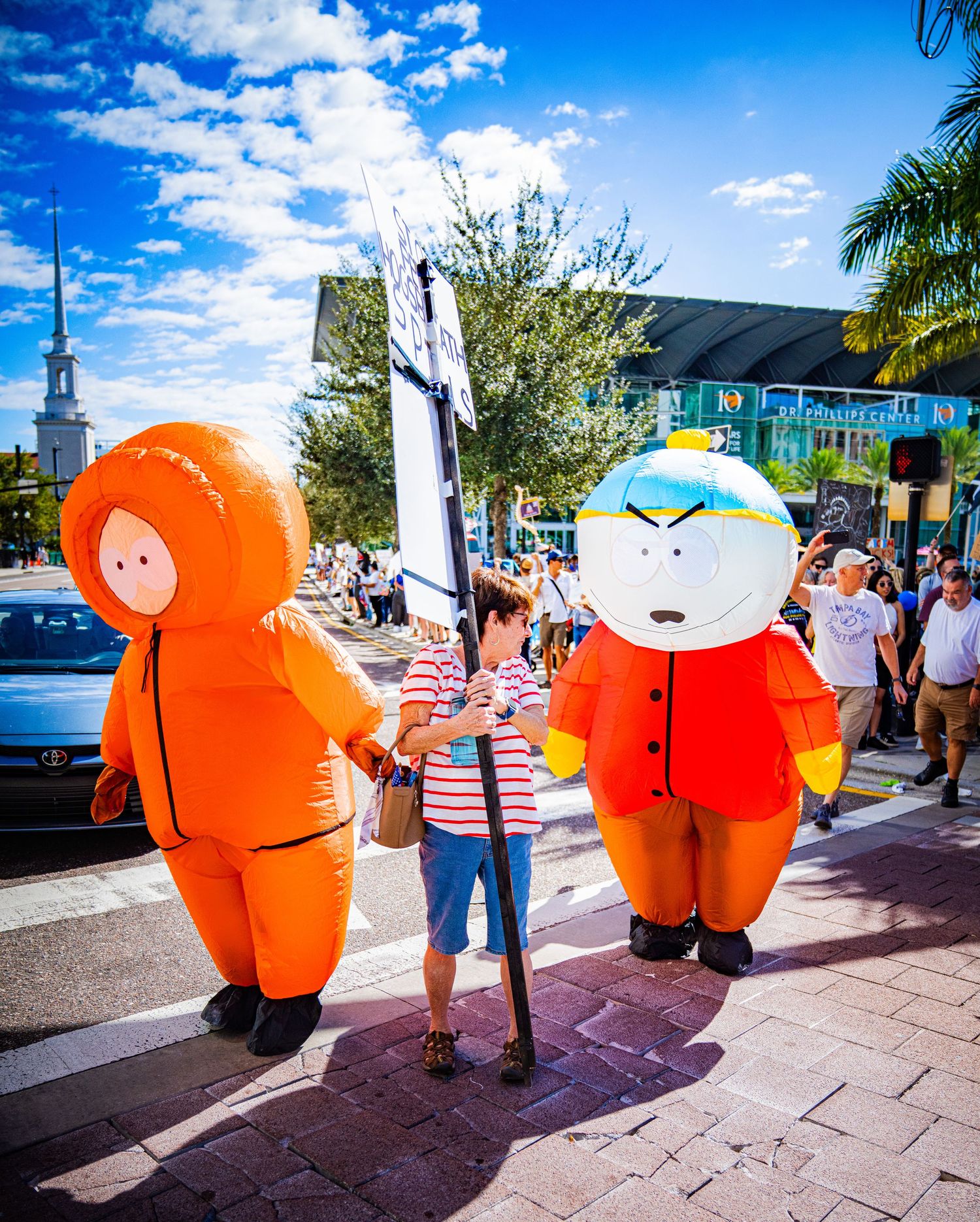 Inflatable orange characters on city sidewalk during public event with blue sky overhead.
