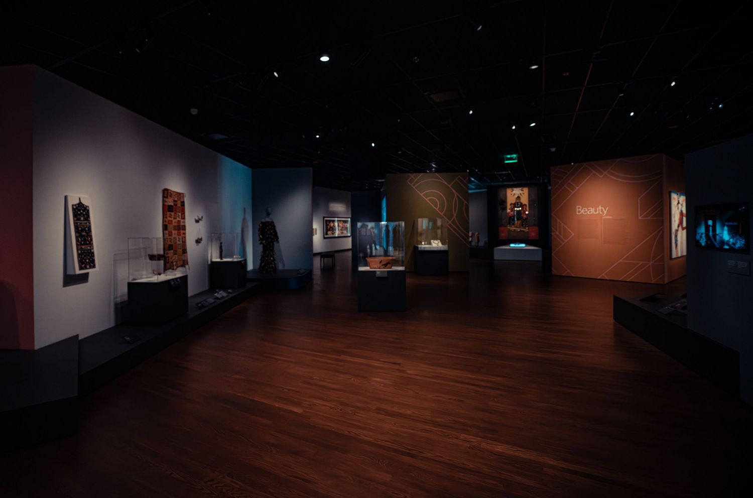 Dark museum gallery with wooden floors displays illuminated artworks on walls in a dimly lit exhibition space.