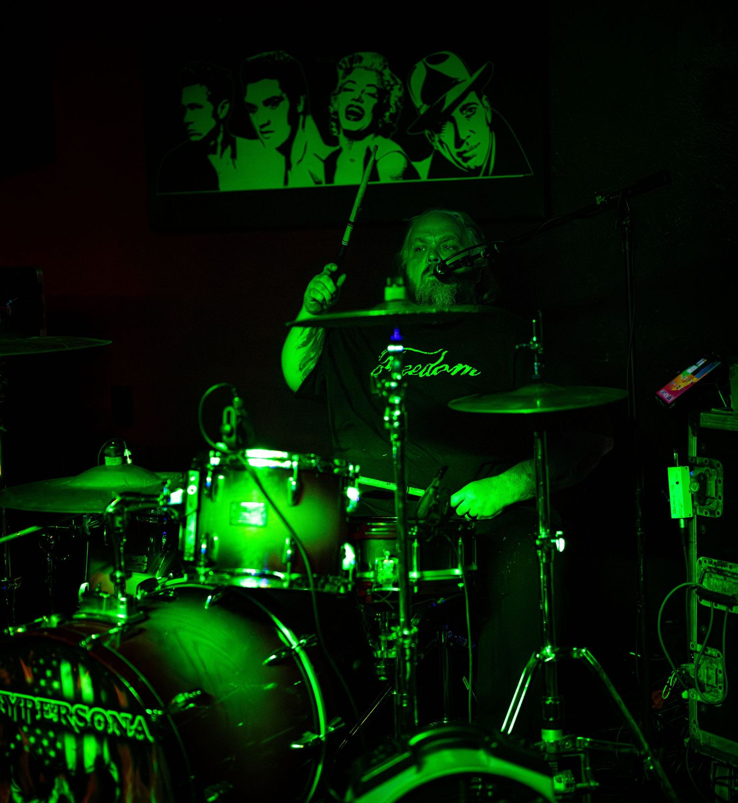 Drummer performing on stage illuminated by dramatic green lighting during a live music show.