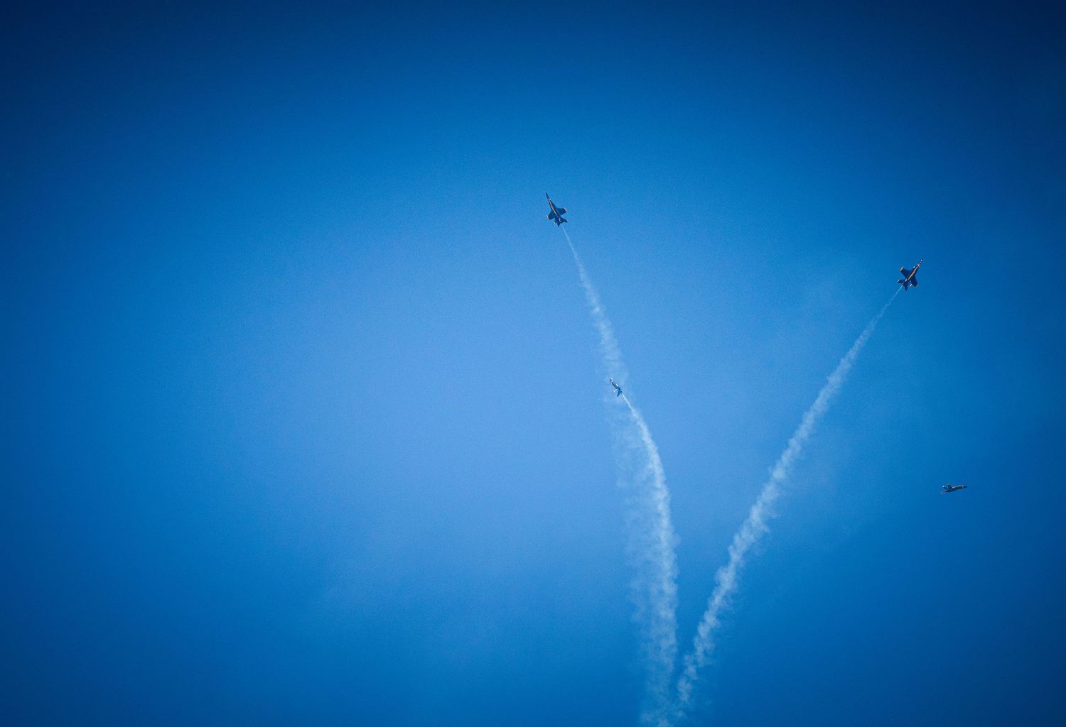 Military aircraft create symmetrical vapor trails across deep blue sky during airshow performance.