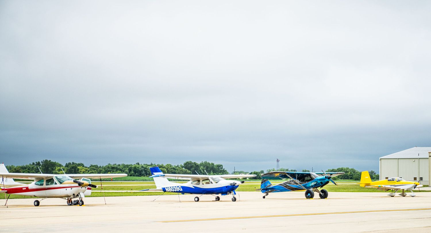 Small aircraft lined up on an airport tarmac under overcast skies.