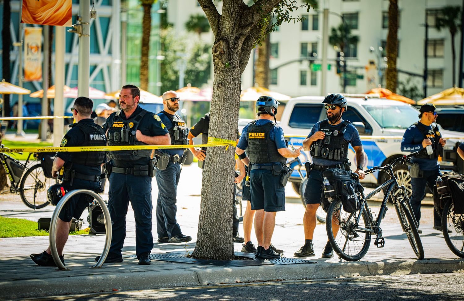 Police officers with bikes gather behind yellow caution tape on a city street.