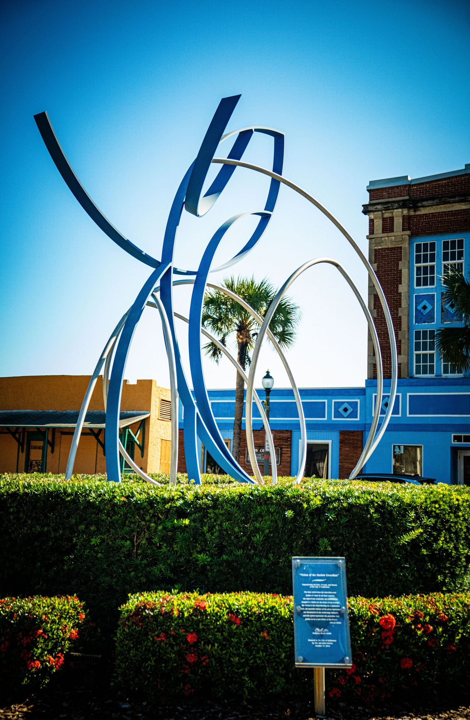 Modern blue metal sculpture installation against bright sky creates dynamic architectural interest in garden setting.