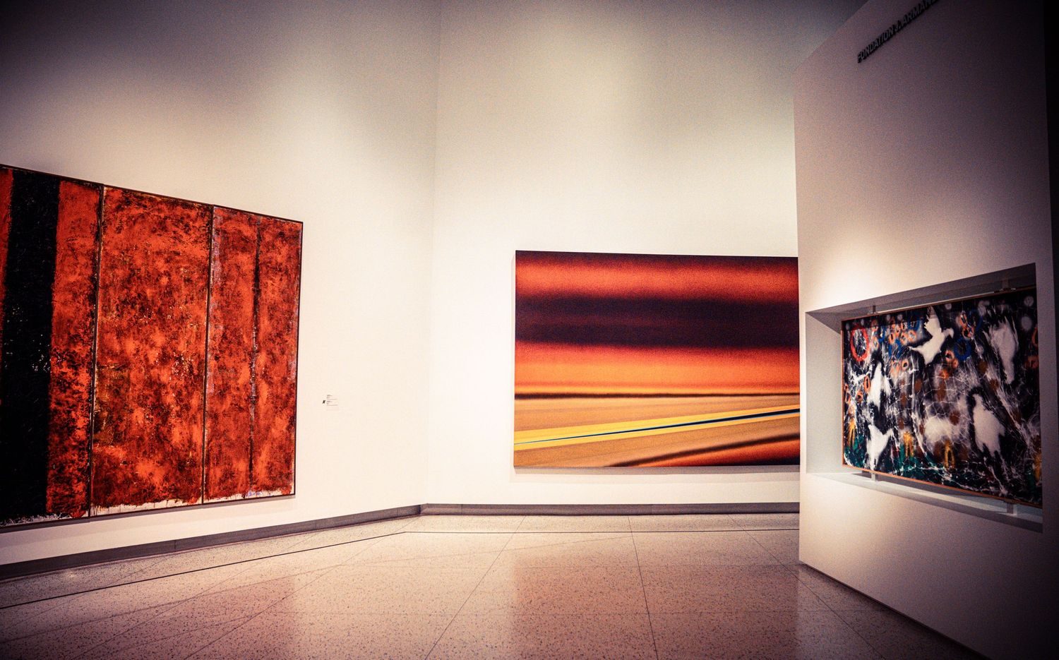 Gallery interior with white walls displaying large format artworks in minimalist setting.