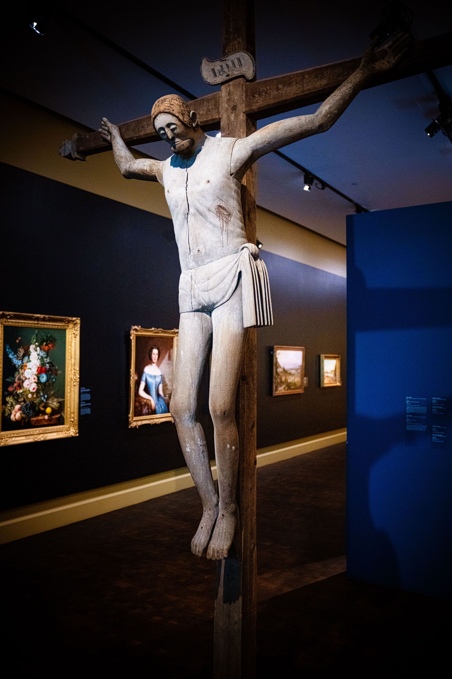 Museum gallery with religious sculptures displayed against dark blue walls.