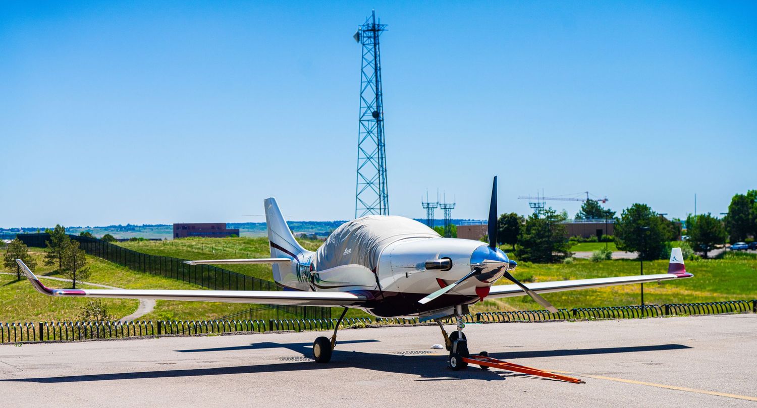 Small aircraft lined up on runway with hangars and control tower in background.