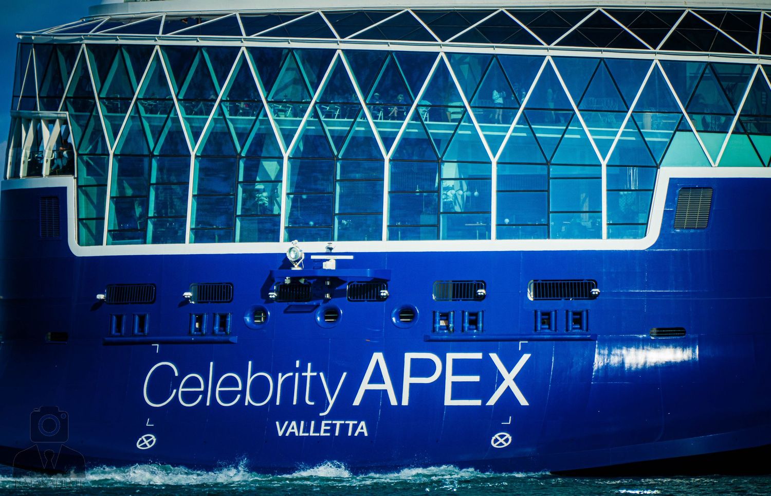 Modern cruise ship exterior lit up in blue lights with 'Celebrity APEX' signage visible.