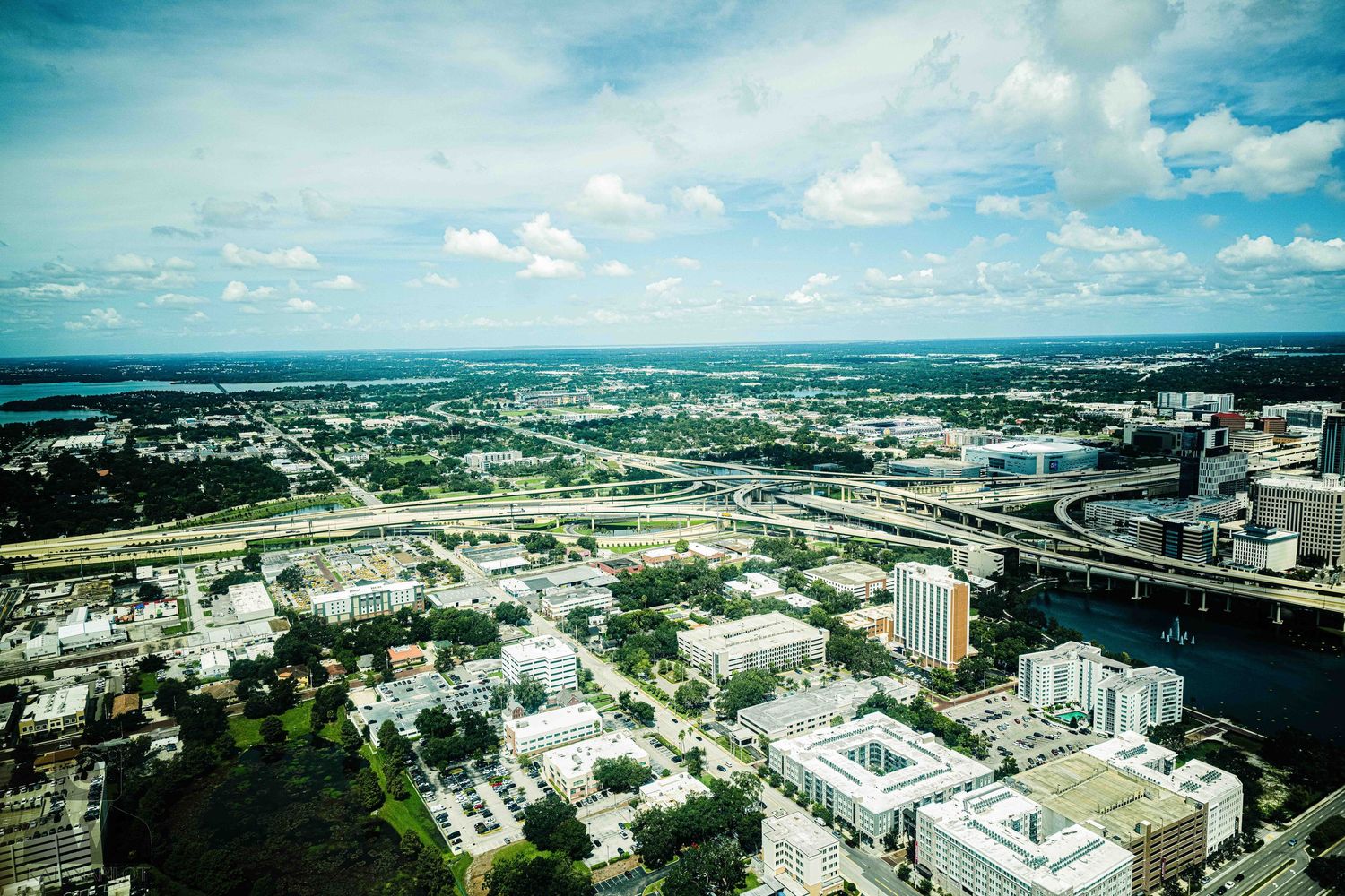 Aerial panoramic view of an urban cityscape with modern buildings and highways under a bright blue sky.