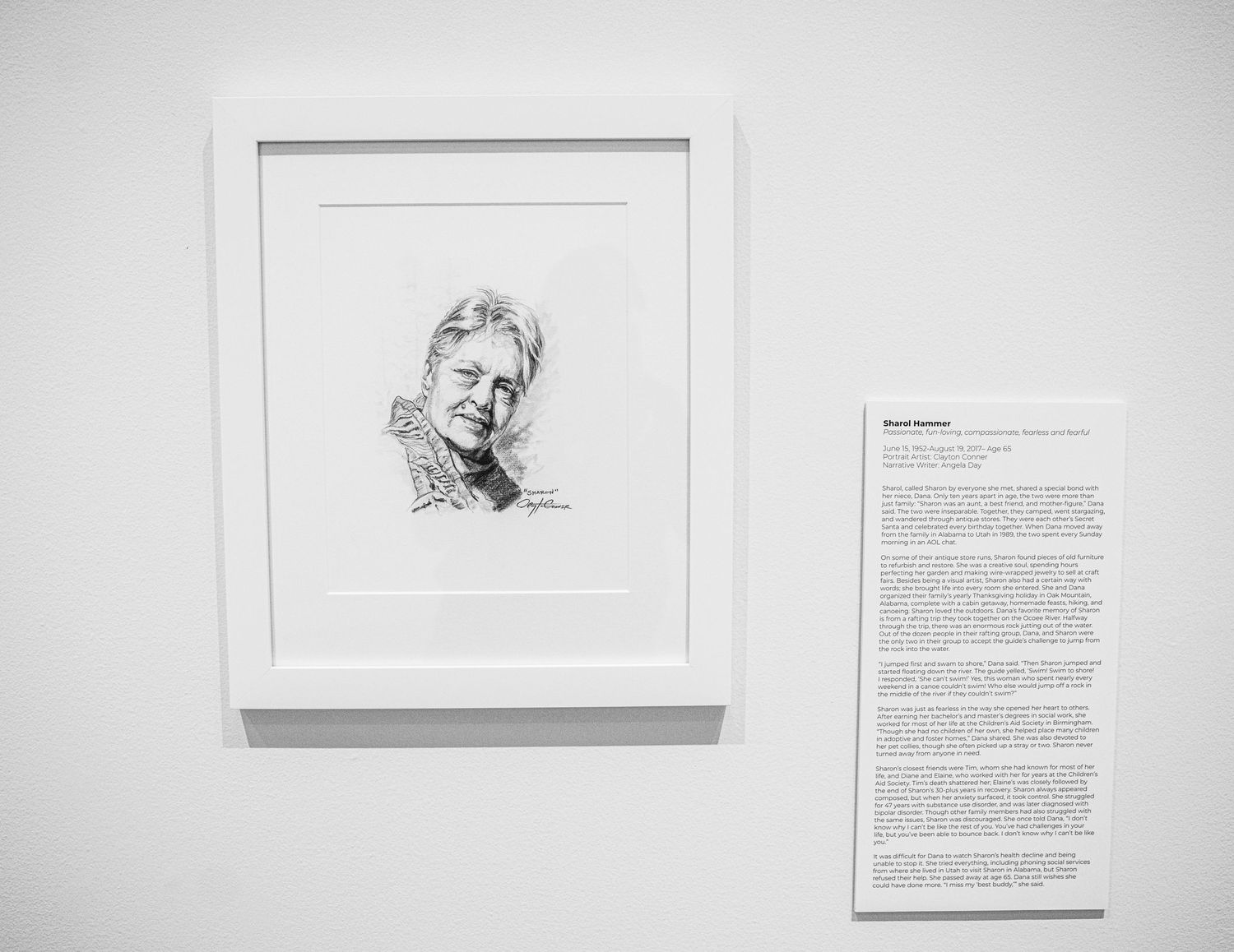 Gallery installation of framed portrait drawings with text panels mounted on white walls.