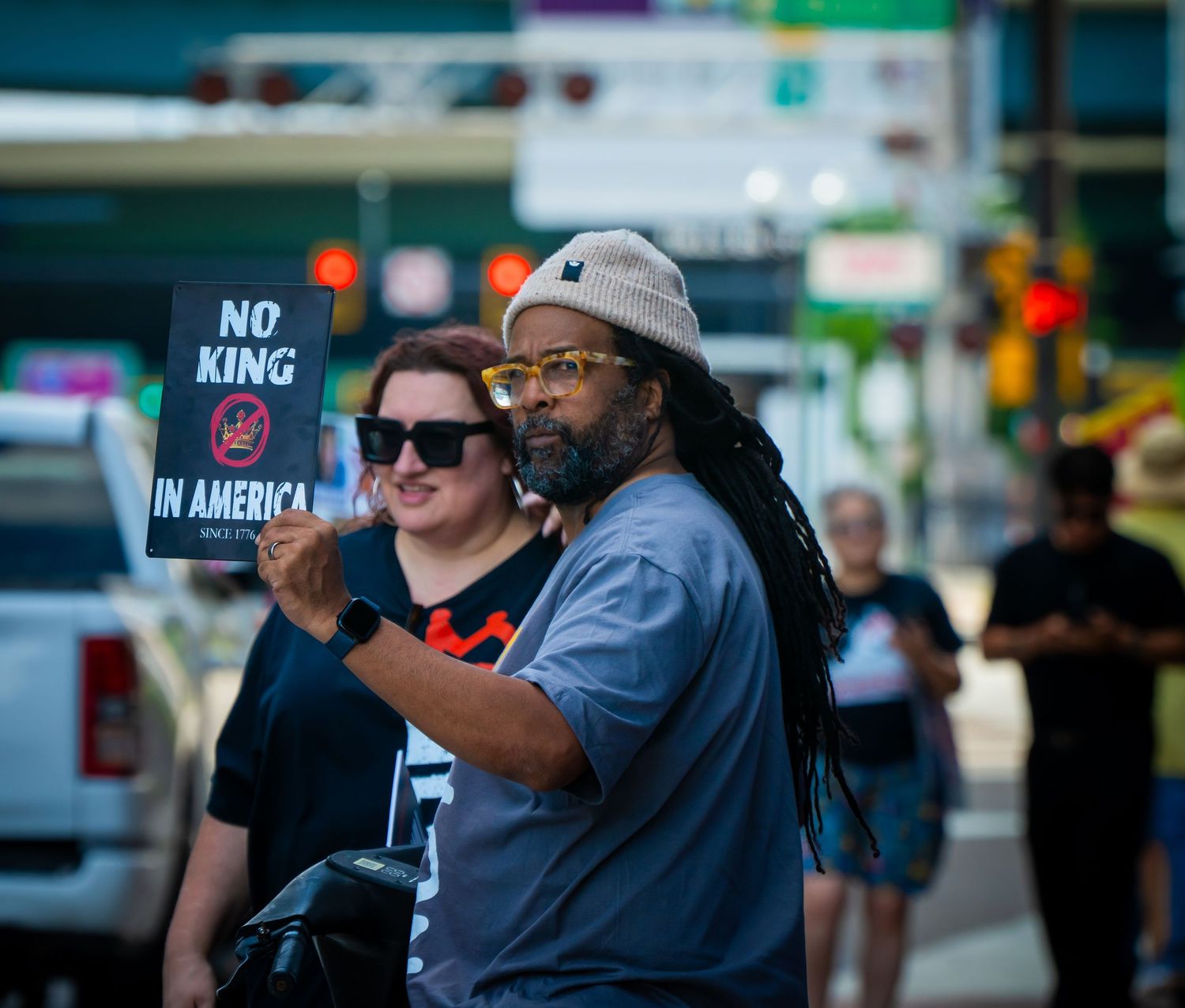 A crowd of demonstrators holds protest signs while marching through an urban area on a sunny day.