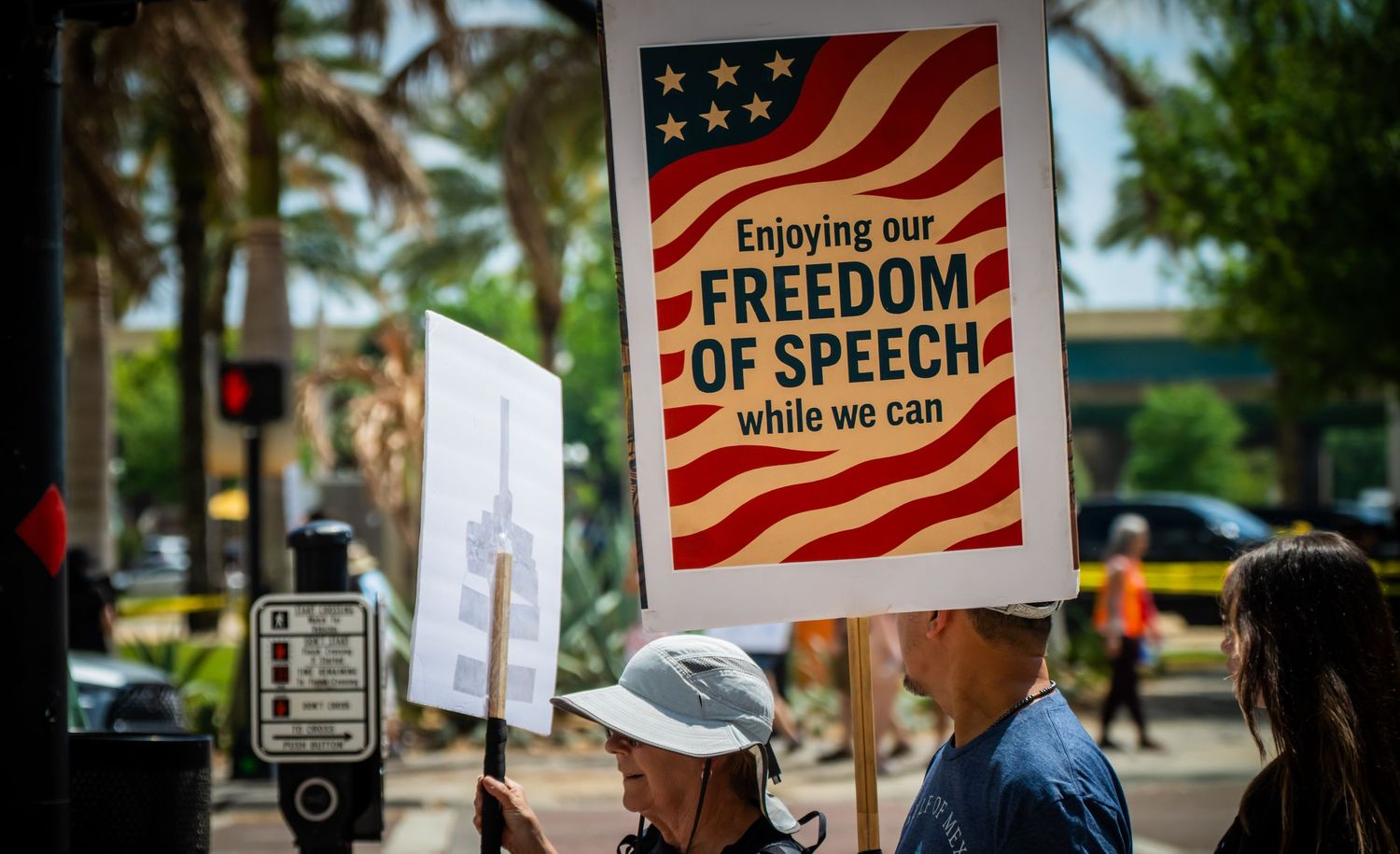 Protesters hold signs about freedom of speech with American flag imagery during a demonstration.