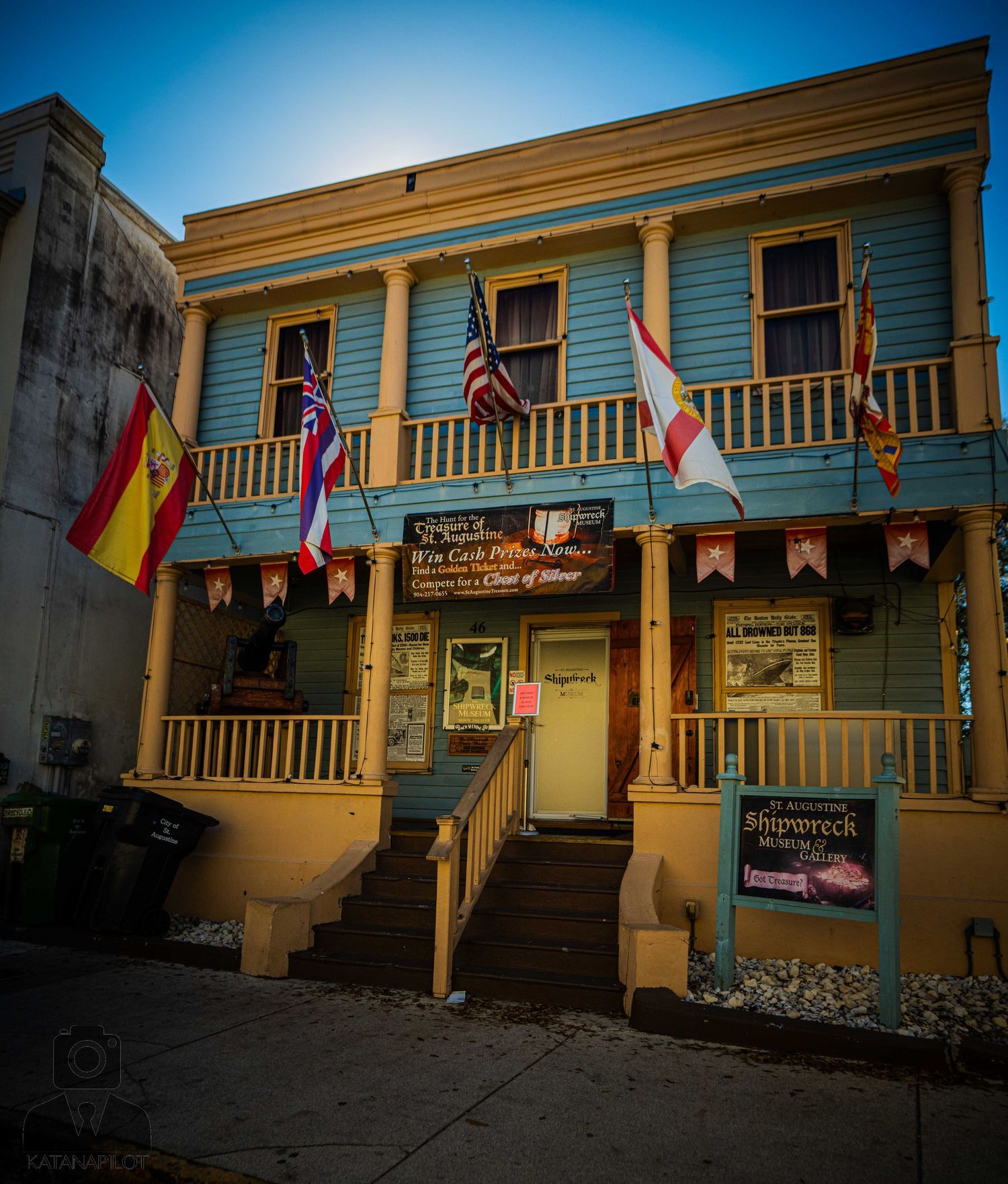 Historic building with multiple international flags and a wooden balcony in a coastal town during sunset.