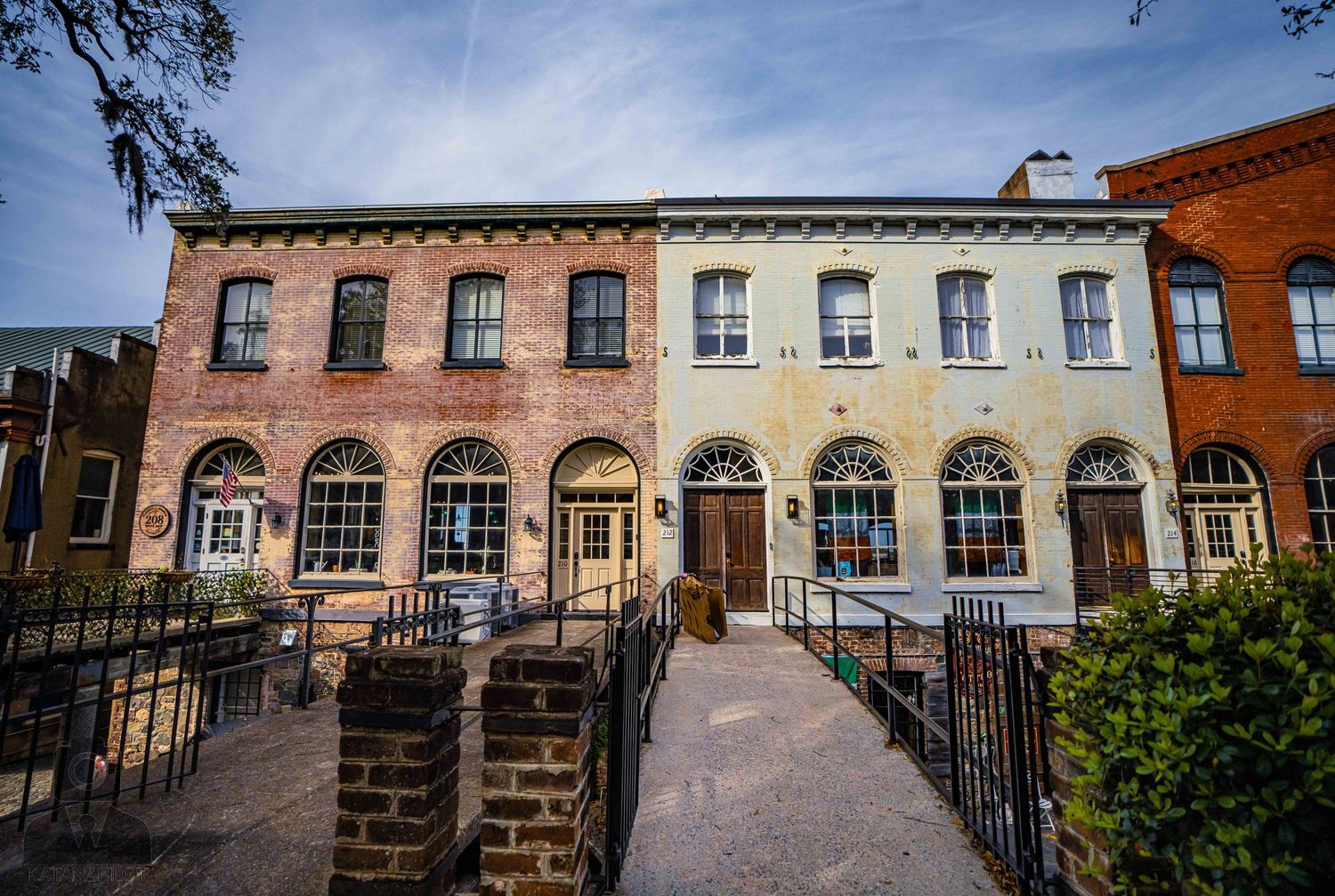 Row of historic colonial buildings with large windows and iron fencing along a street in Savannah's historic district.