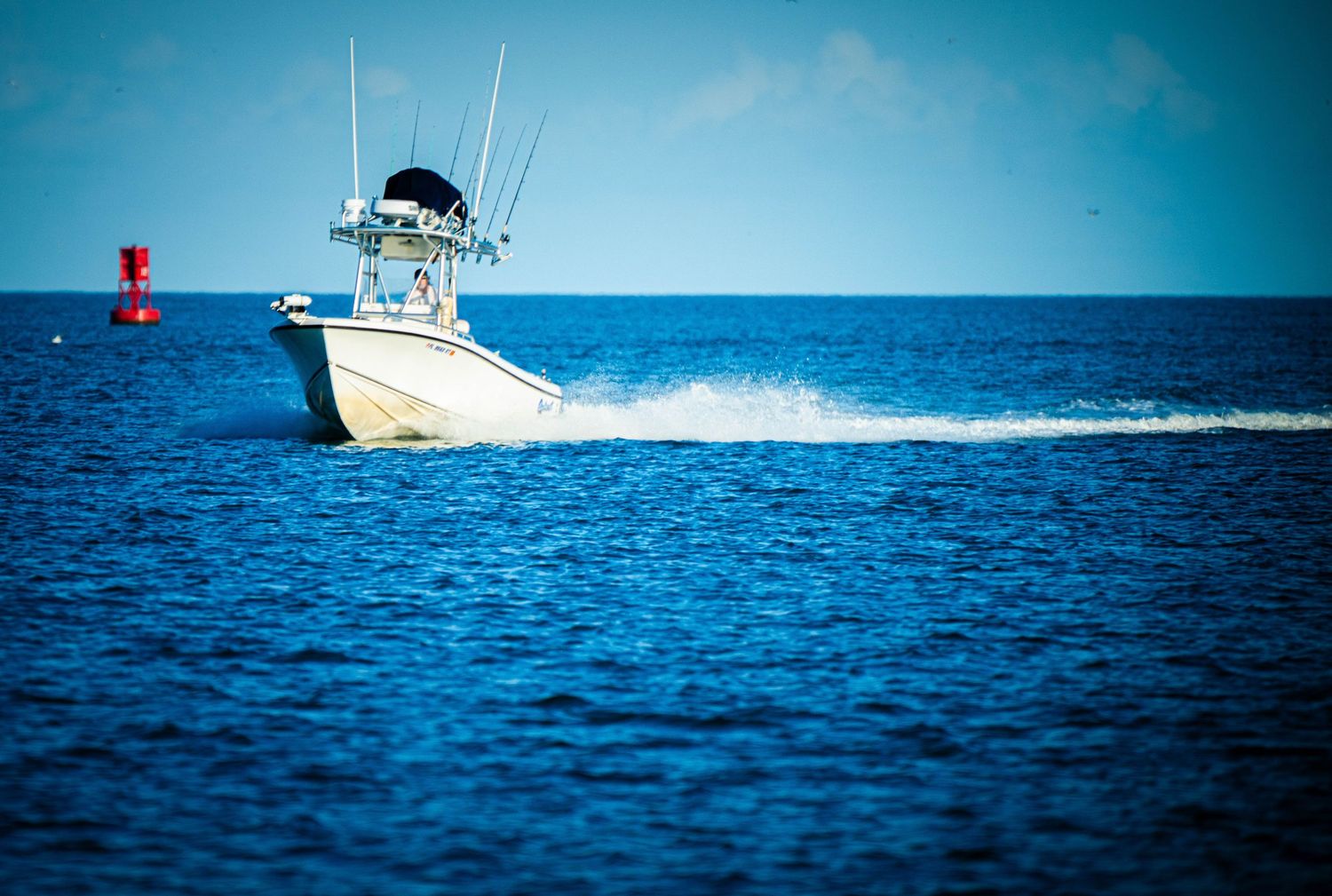 A white fishing boat cruises across bright blue ocean waters leaving a wake behind it.
