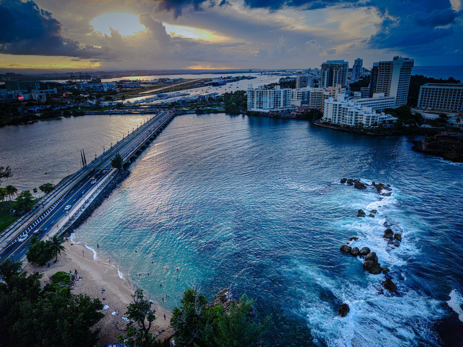 Aerial panorama of Honolulu's coastline showing turquoise waters, beach resorts, and mountain backdrop at dusk.
