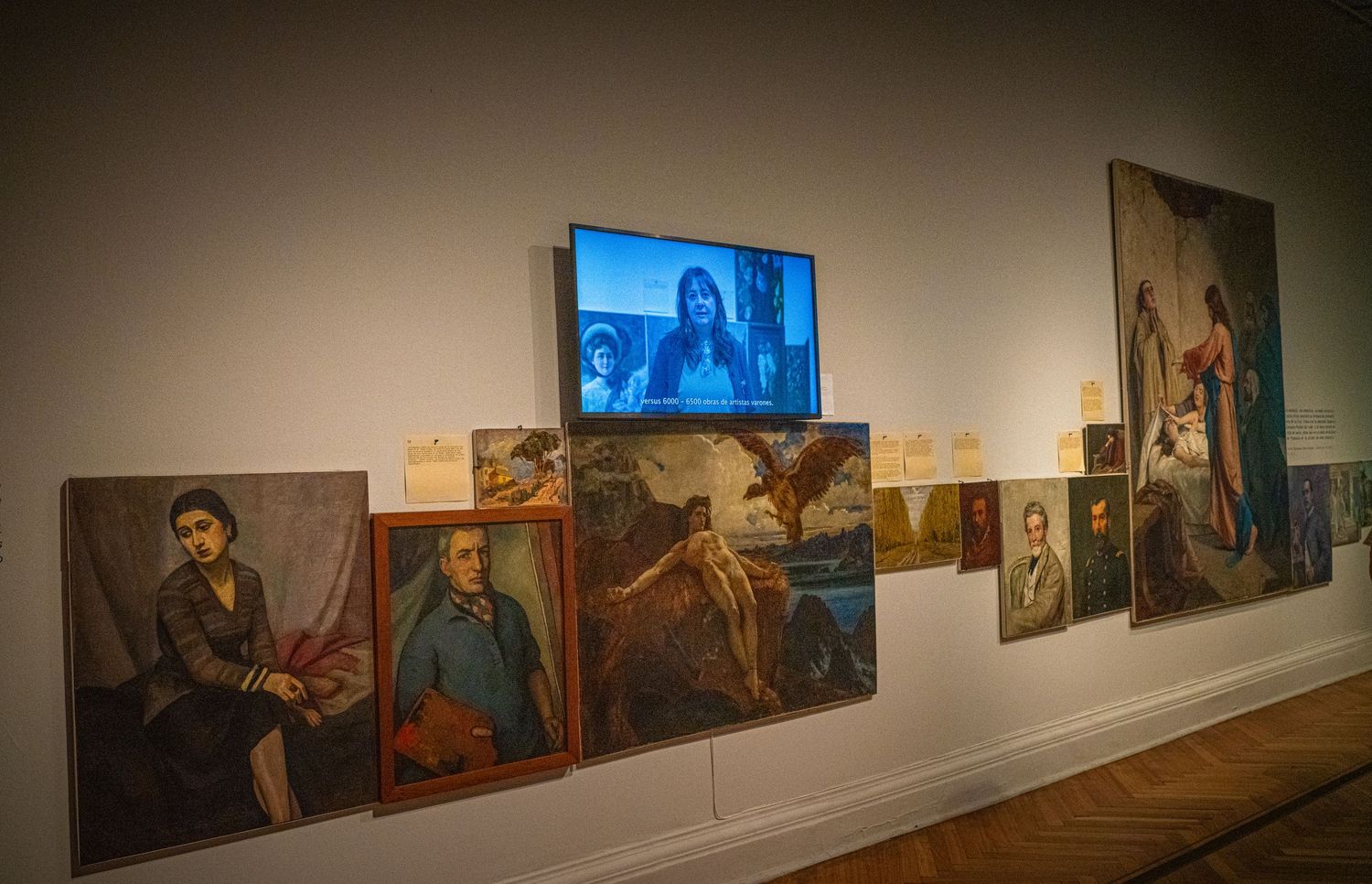 Museum wall display featuring multiple paintings and a central digital screen.