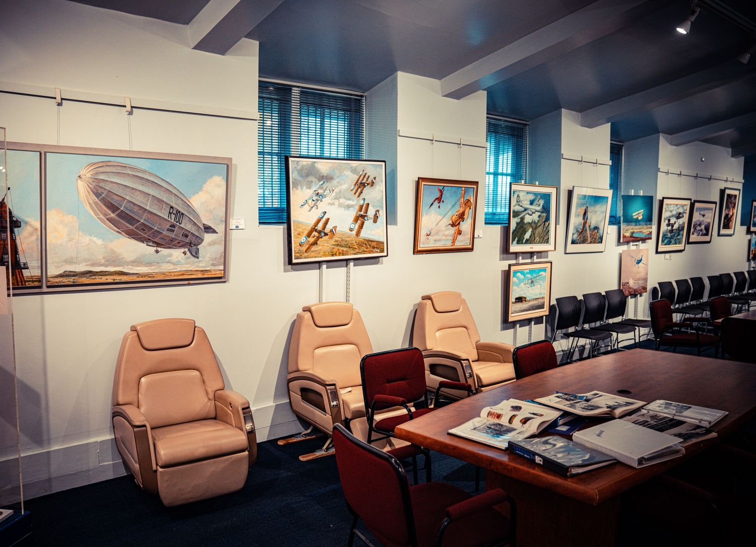 Aviation museum gallery with tan leather chairs and vintage aircraft paintings on display.