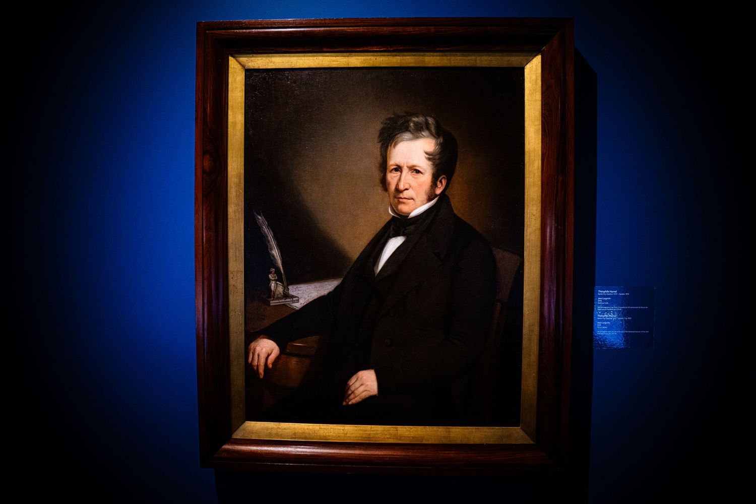 Historic portrait paintings displayed in gold frames against a dark blue gallery wall.