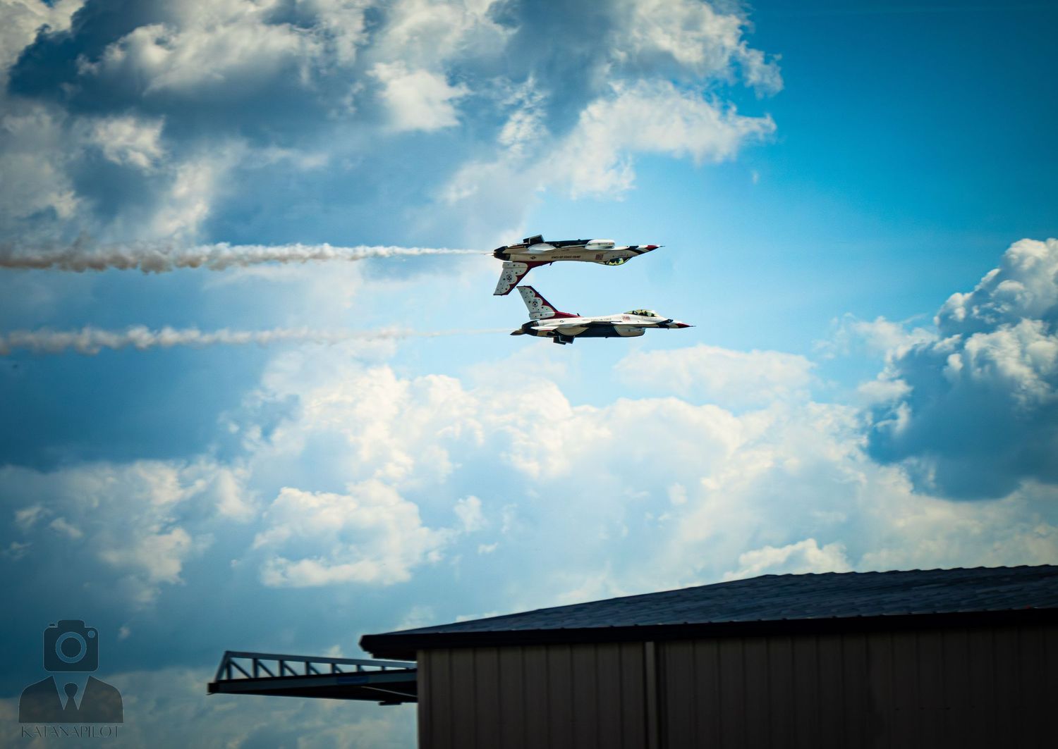 Two U.S. Air Force Thunderbirds perform a dramatic crossing maneuver leaving white smoke trails against a blue cloudy sky.