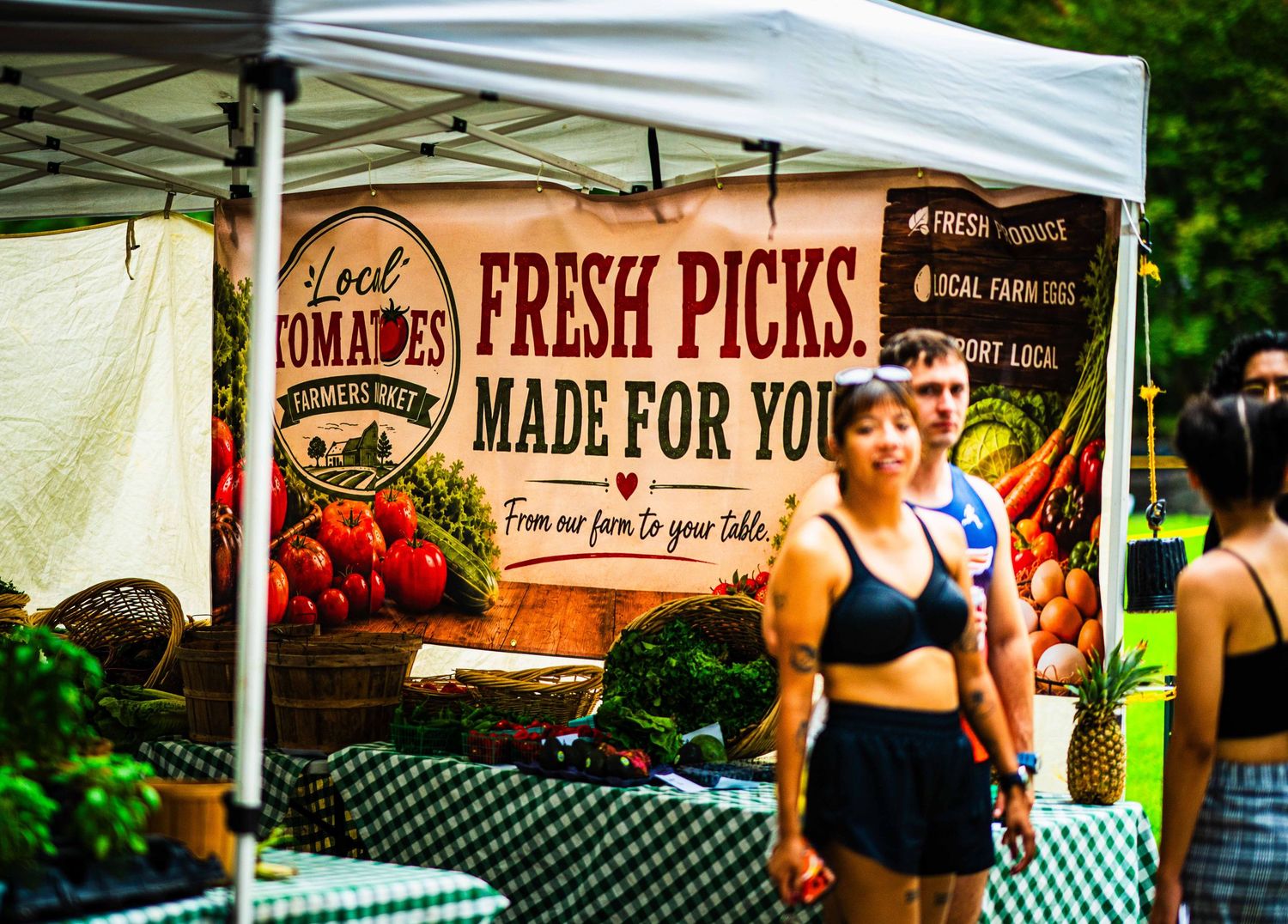 Fresh produce stand at a farmers market with a colorful banner reading Fresh Picks Made For You, Local Tomatoes.