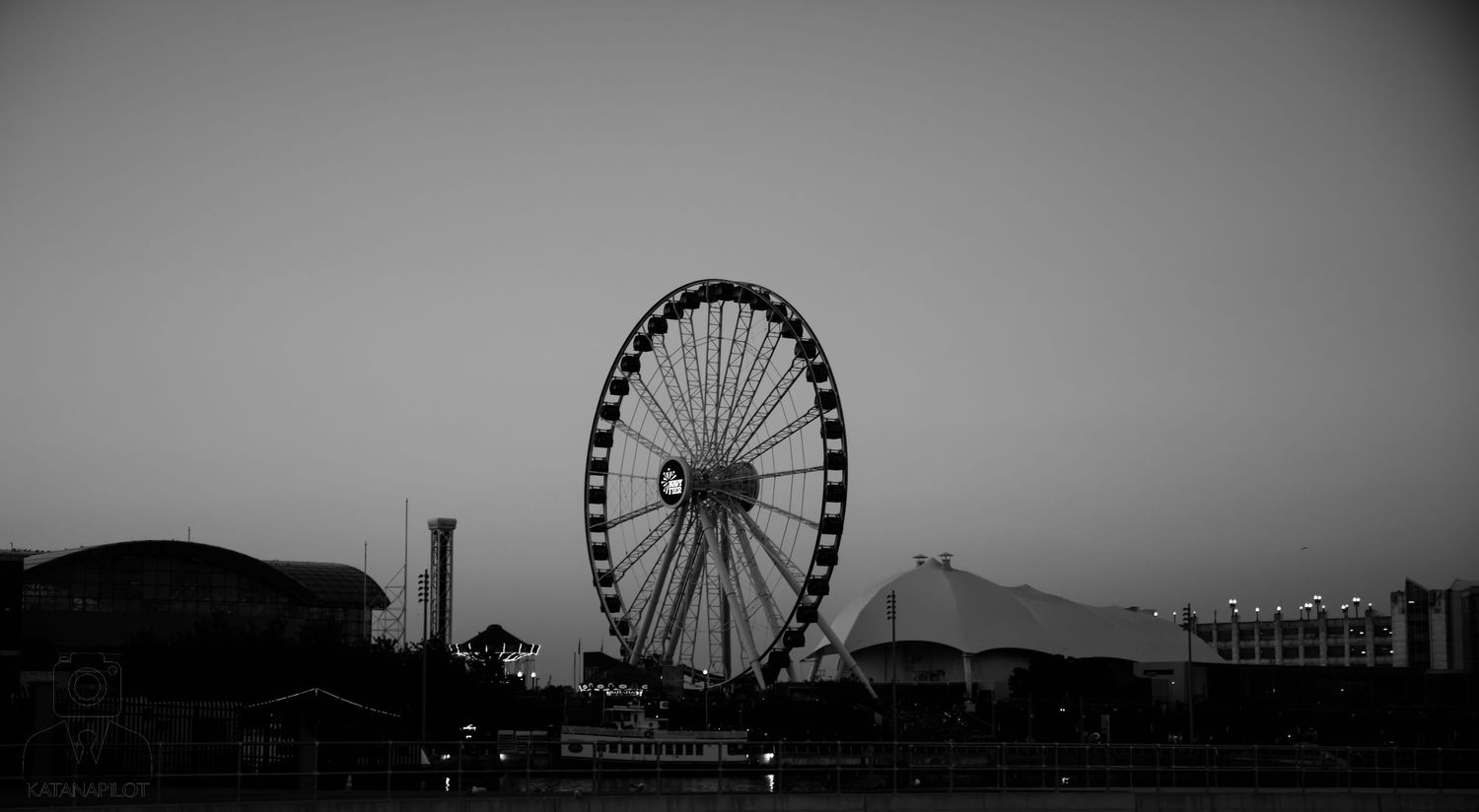 Silhouette of a Ferris wheel and amusement park rides against a dusky sky.