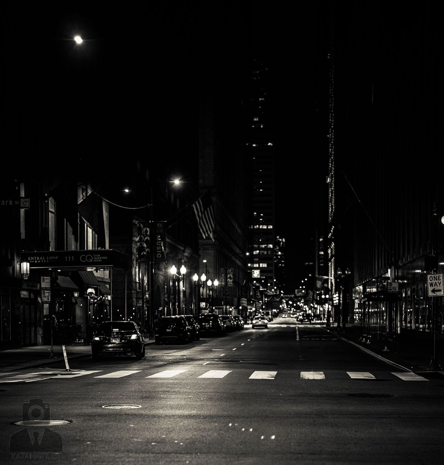 Dark urban street scene at night with glowing streetlights and building silhouettes.