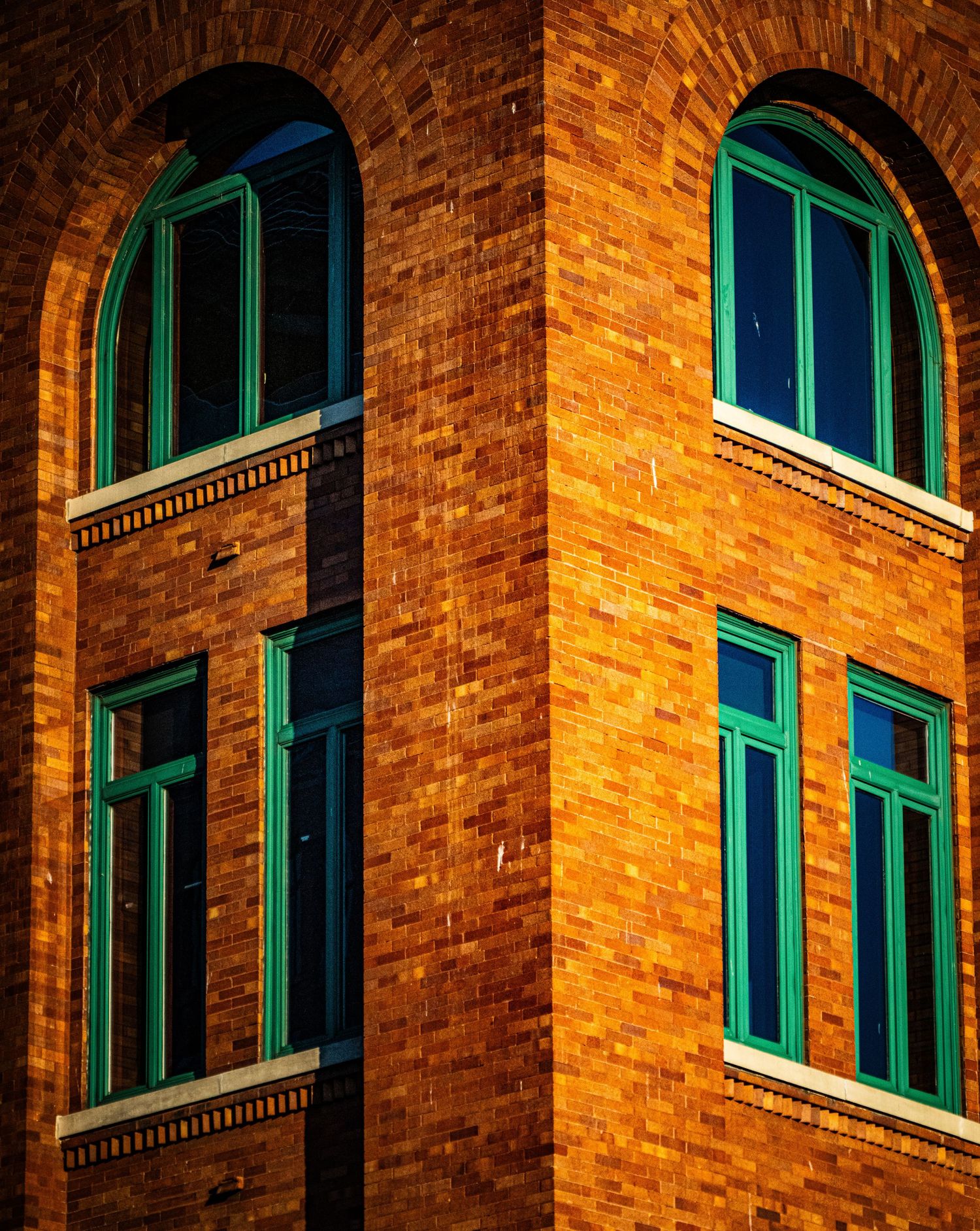 Historic brick building with green-trimmed arched windows in warm lighting.