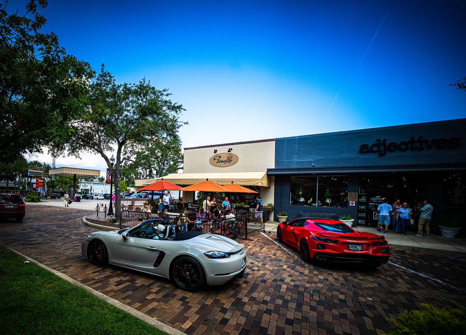 Shopping center parking lot with luxury cars under bright blue sky.
