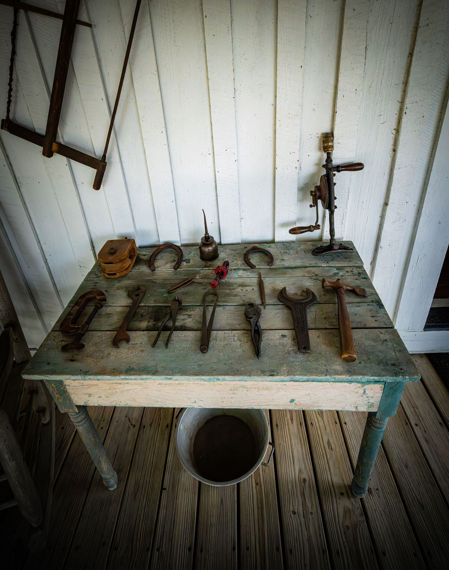 Rustic wooden shelf displaying antique tools and household items against white wall.
