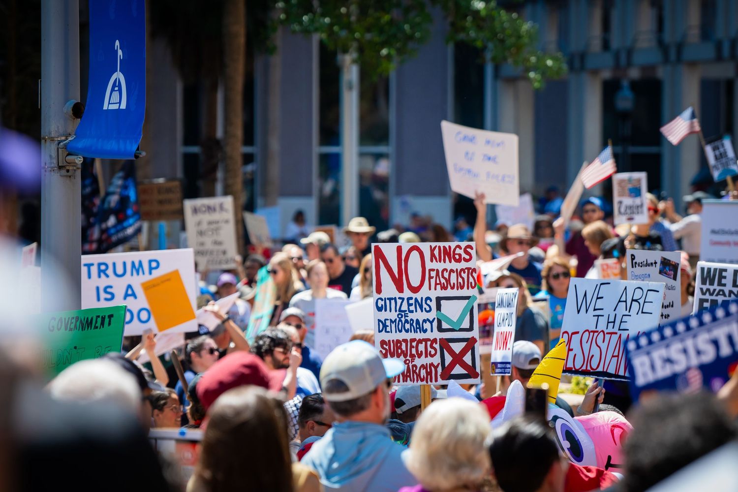Large crowd of protesters holding signs at a political demonstration march through city streets.