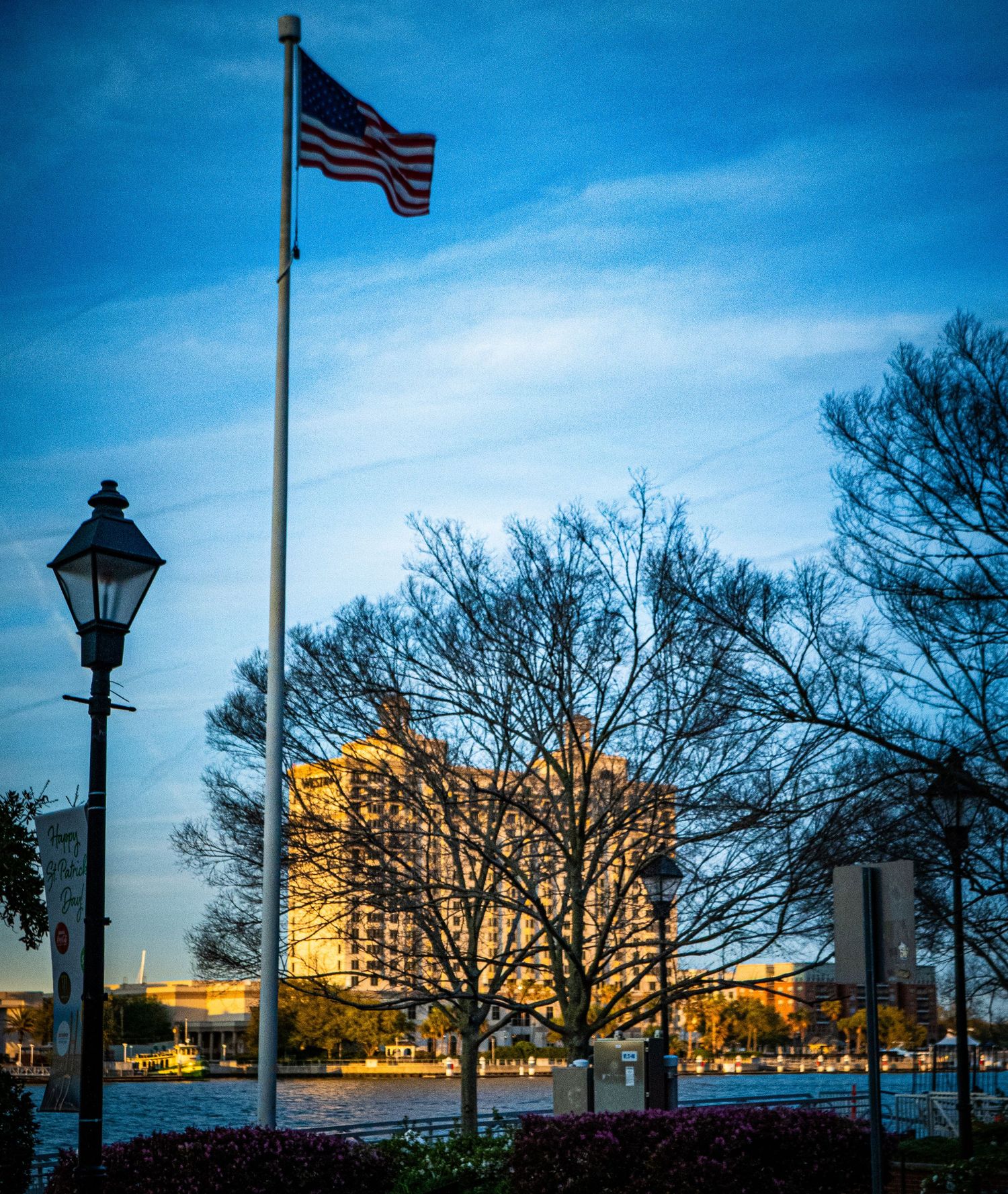 Panoramic cityscape at dusk with American flag and illuminated buildings against a deep blue sky.