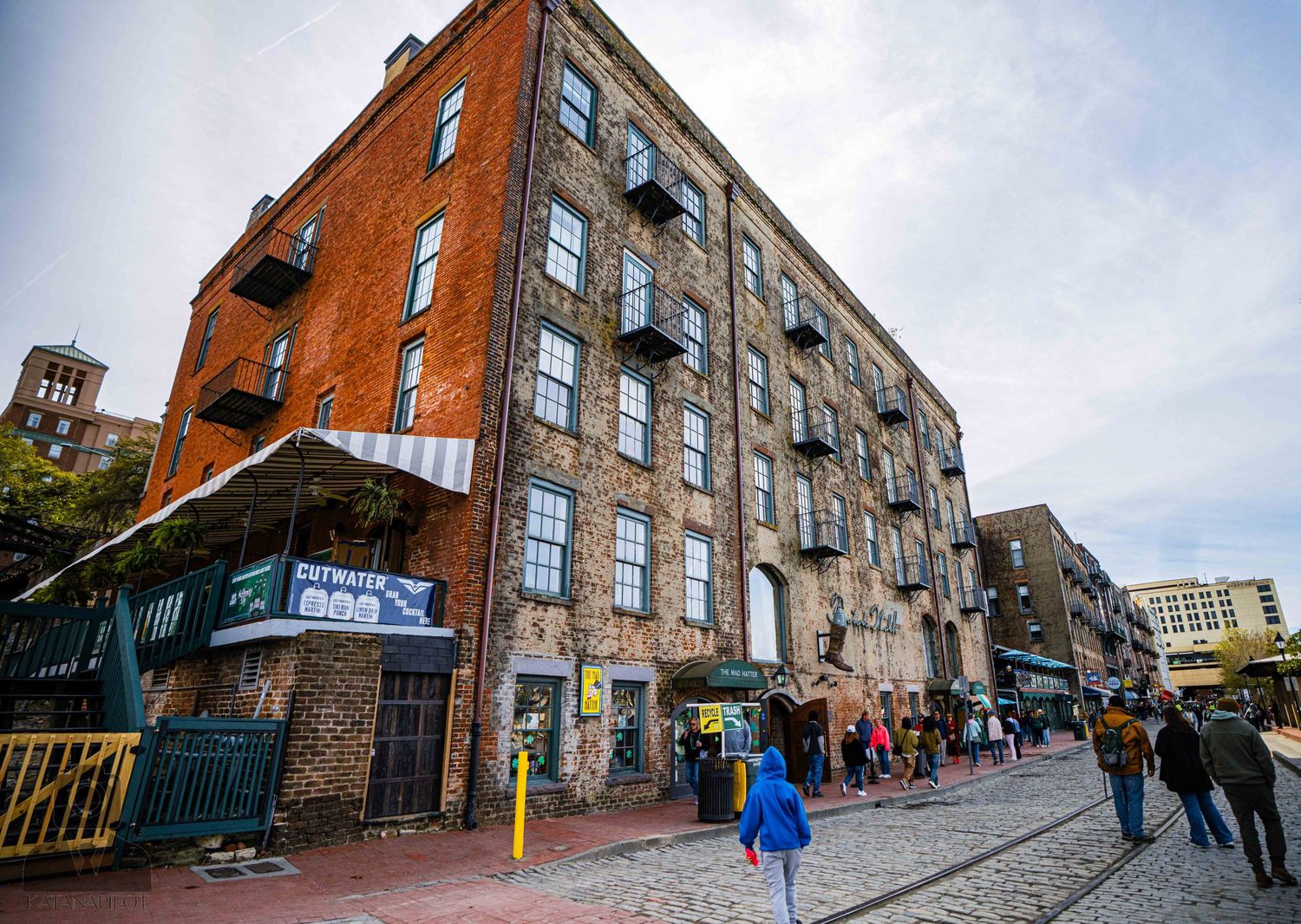 Historic red brick warehouse building with fire escapes and shops at street level on cobblestone road.