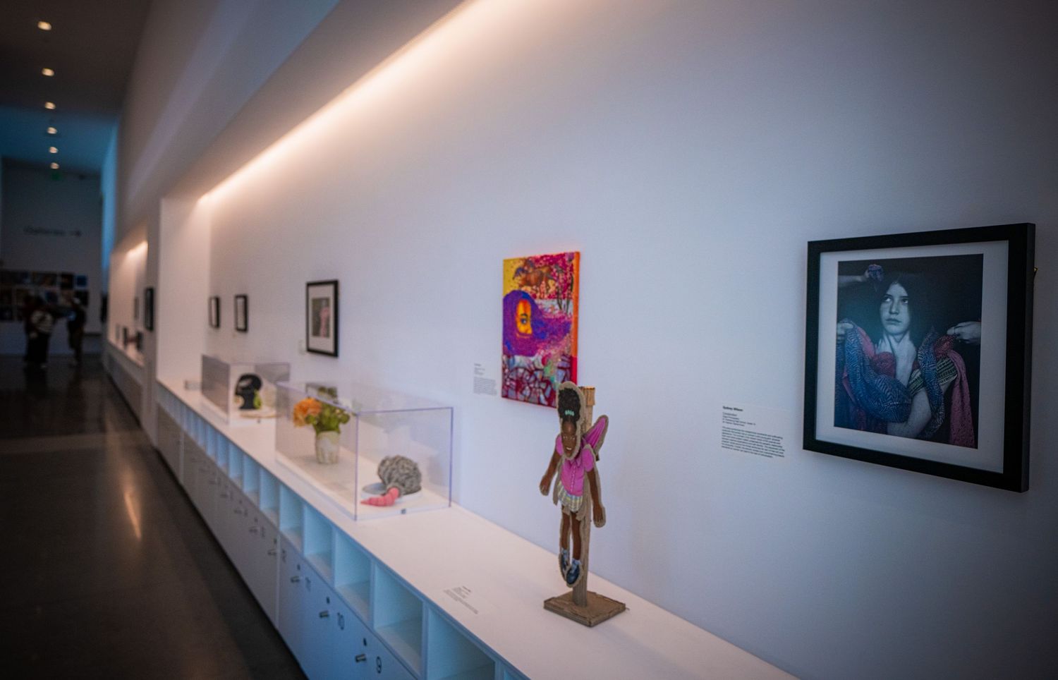 Art gallery interior with white walls displaying framed photographs and sculptures along a narrow hallway.